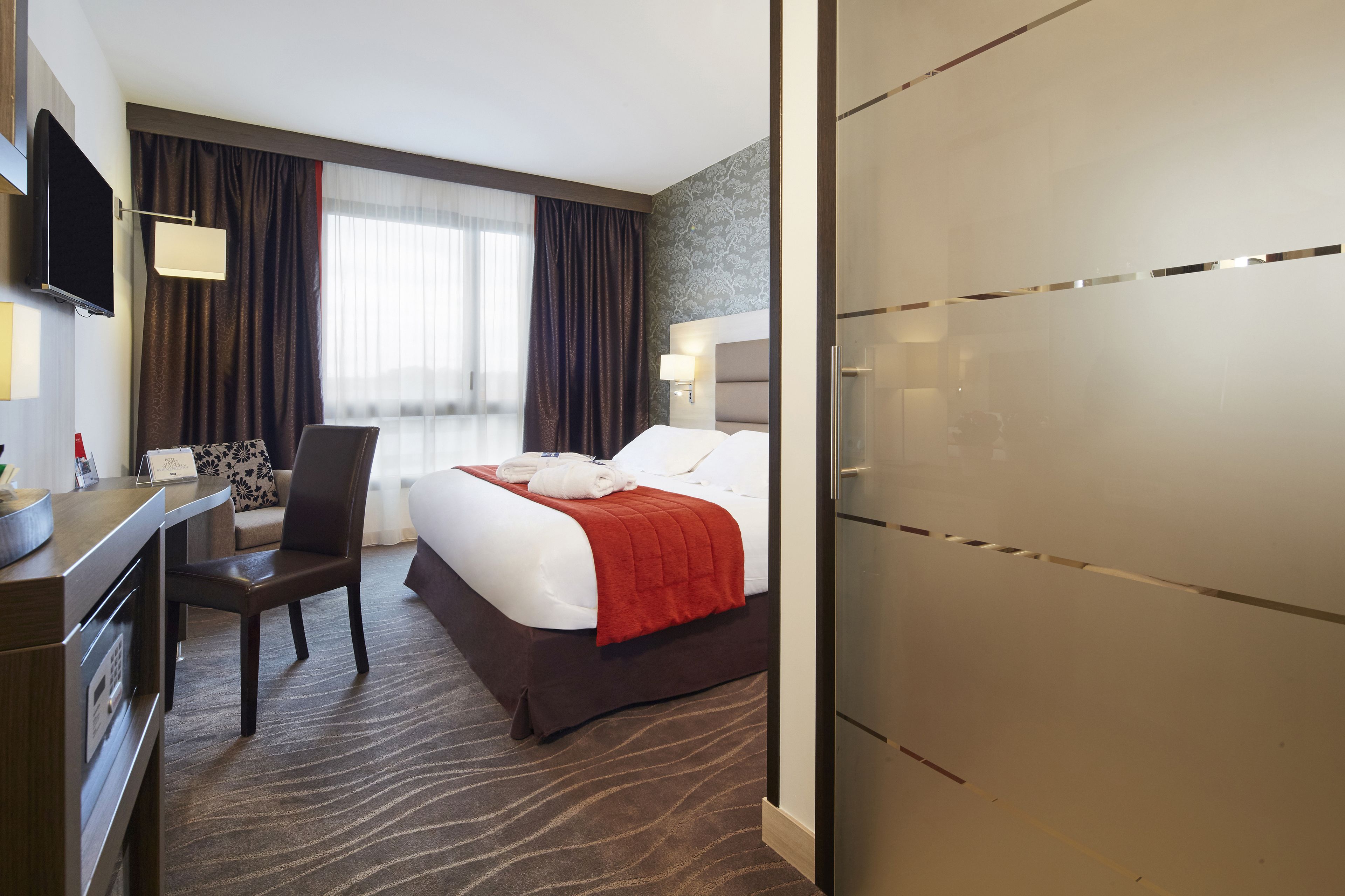 A hotel room with a bed, a desk, a chair, a TV, and a wardrobe.