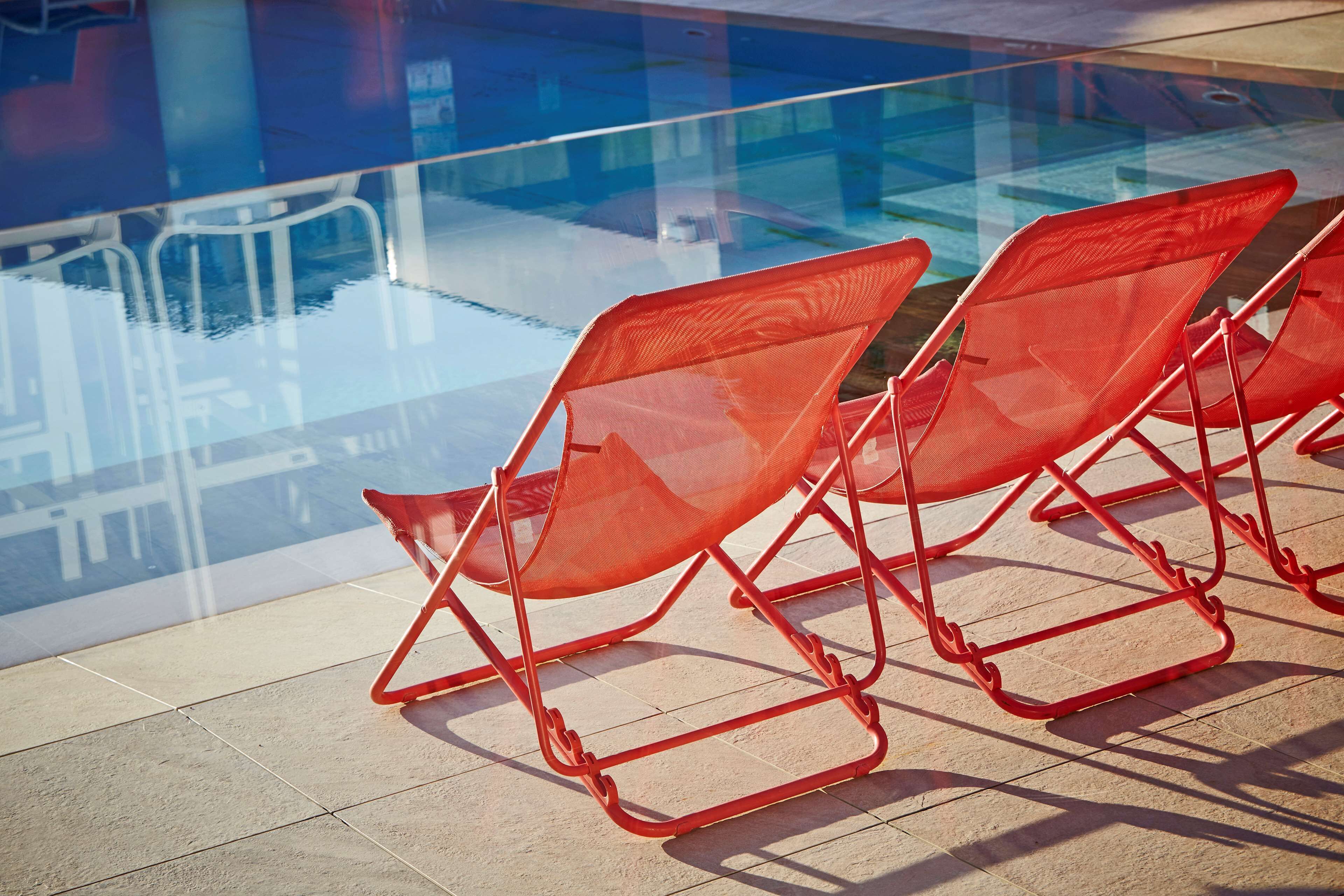 A poolside area with red lounge chairs and a glass barrier.