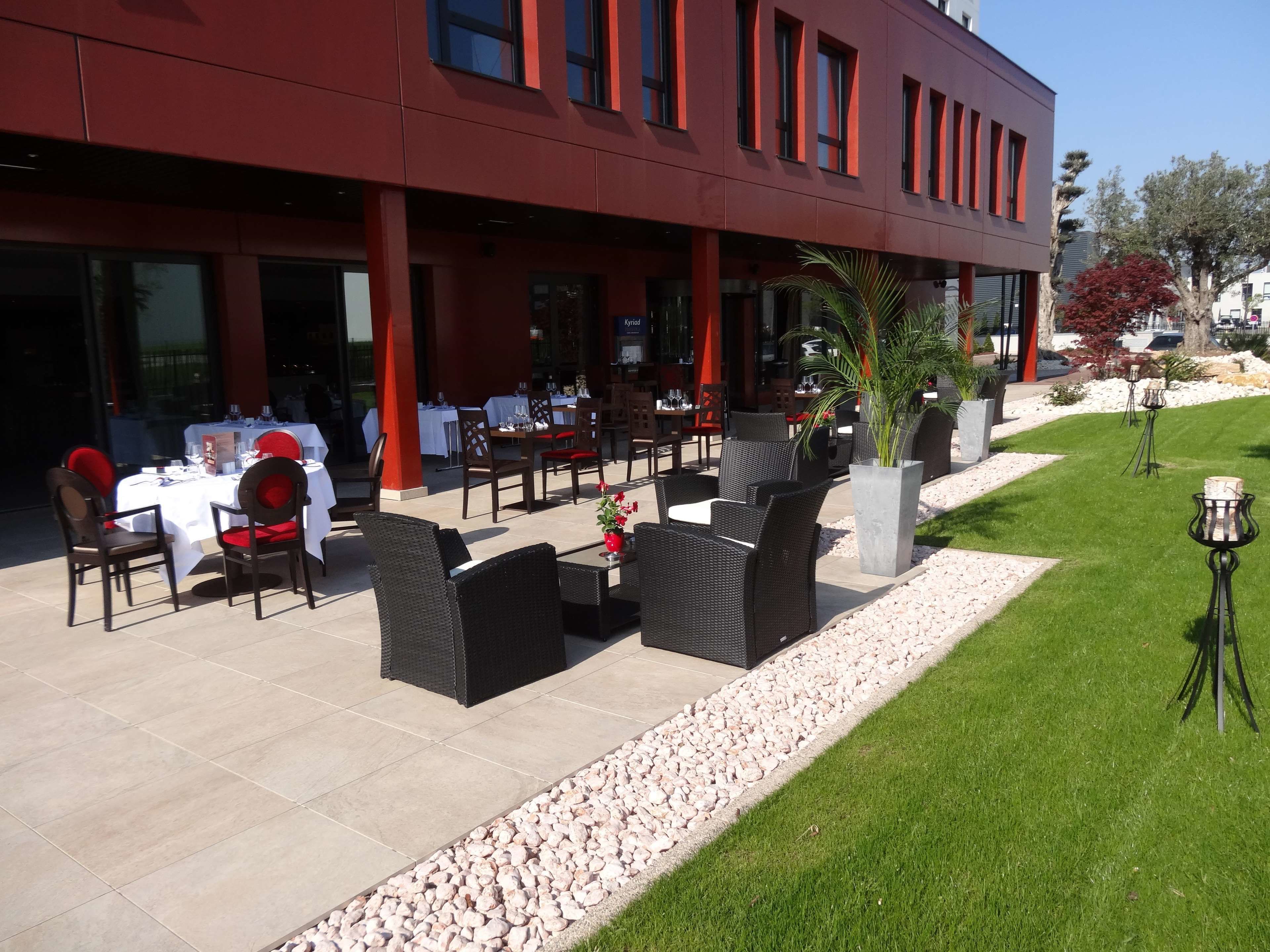 An outdoor dining area with tables and chairs, a grassy lawn, and a modern building in the background.