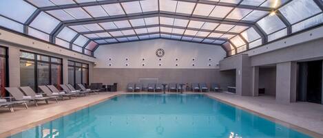 Una piscina con techo de cristal, sillones de descanso y un reloj en la pared.