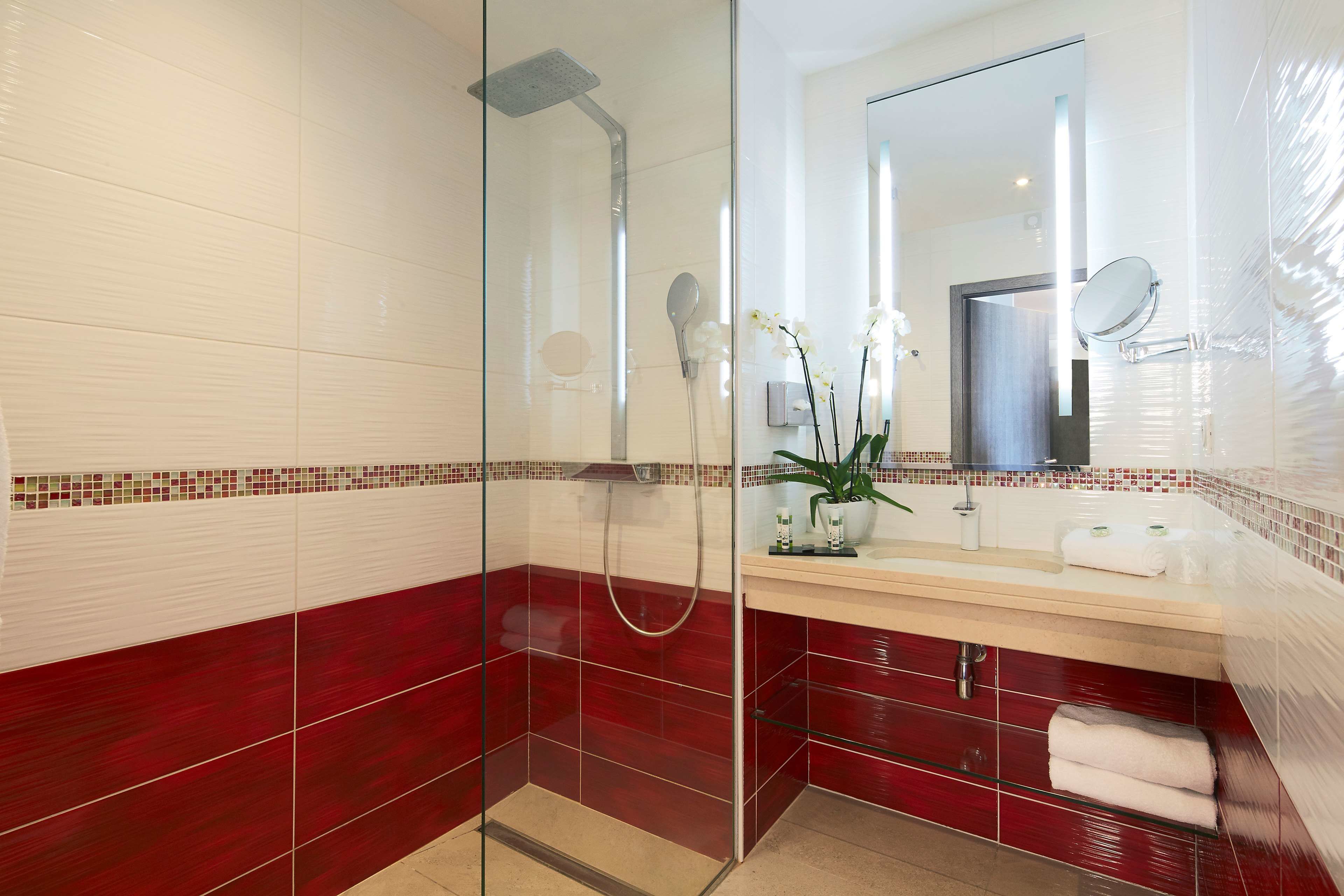 A modern bathroom with a glass-enclosed shower, a vanity with a mirror, and a red-tiled wall.