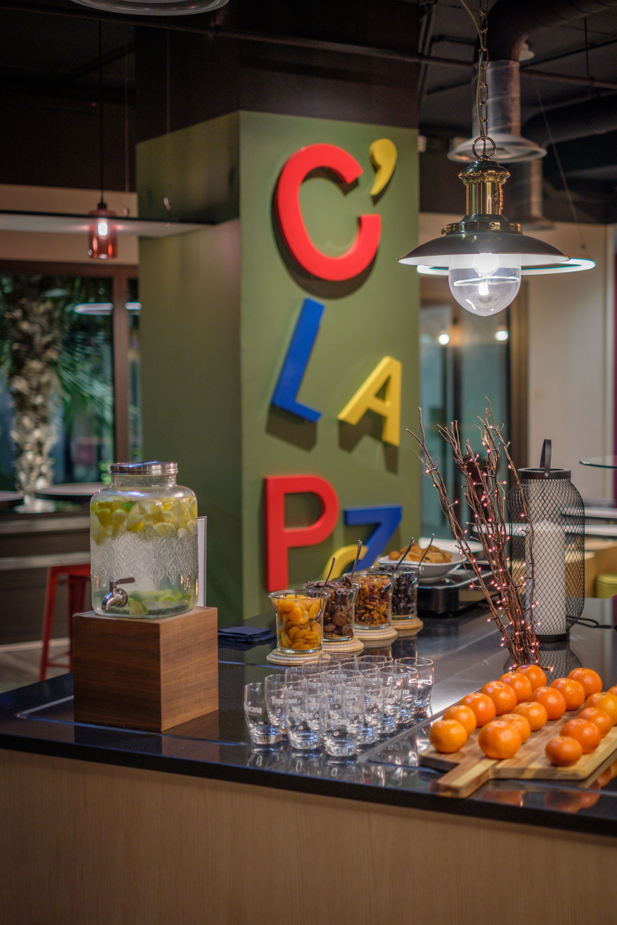 A bar area with a counter, a large jar of pickles, glasses, and a decorative branch.