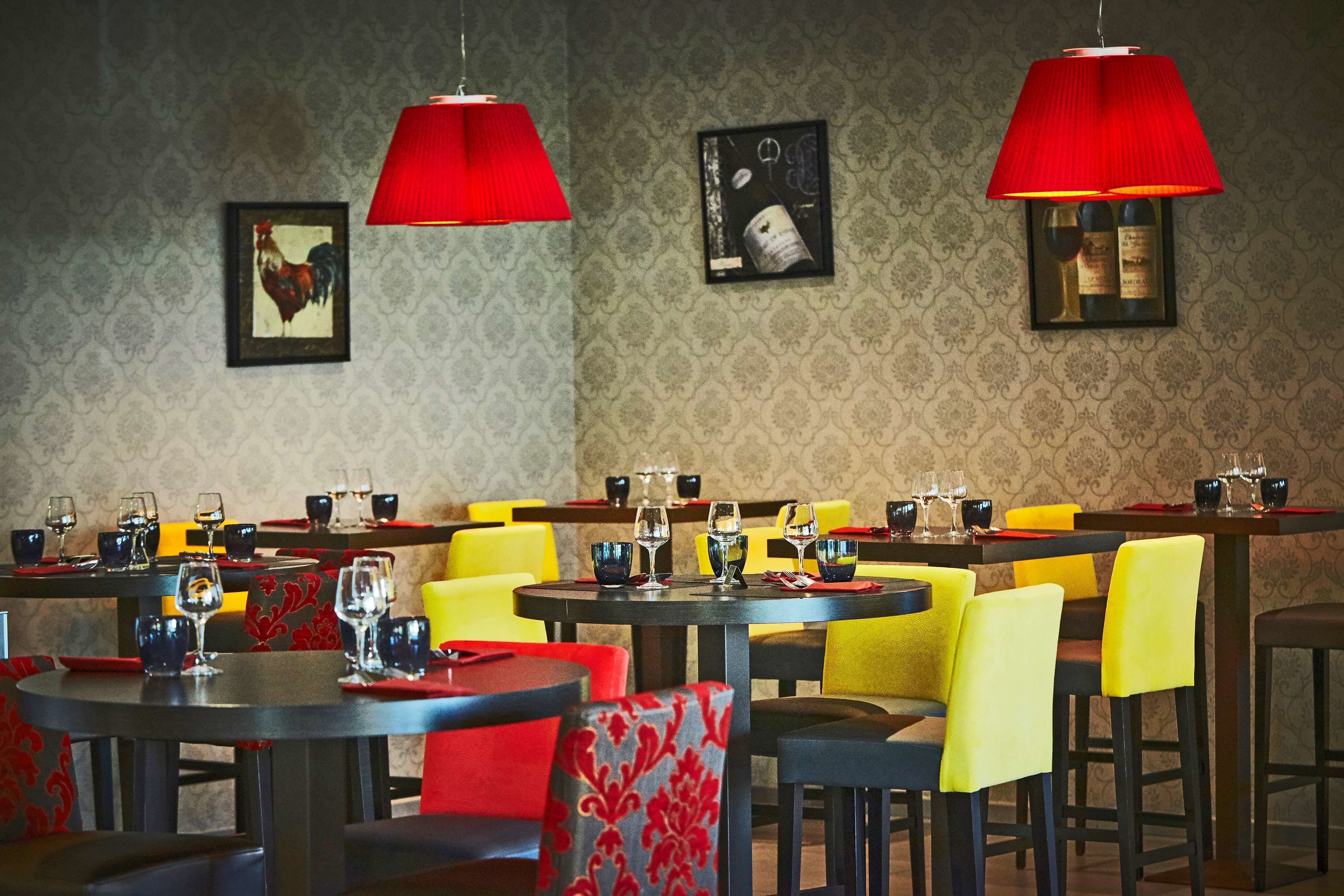 Un restaurant avec des tables rondes, des chaises jaunes et rouges, et des abat-jours rouges.