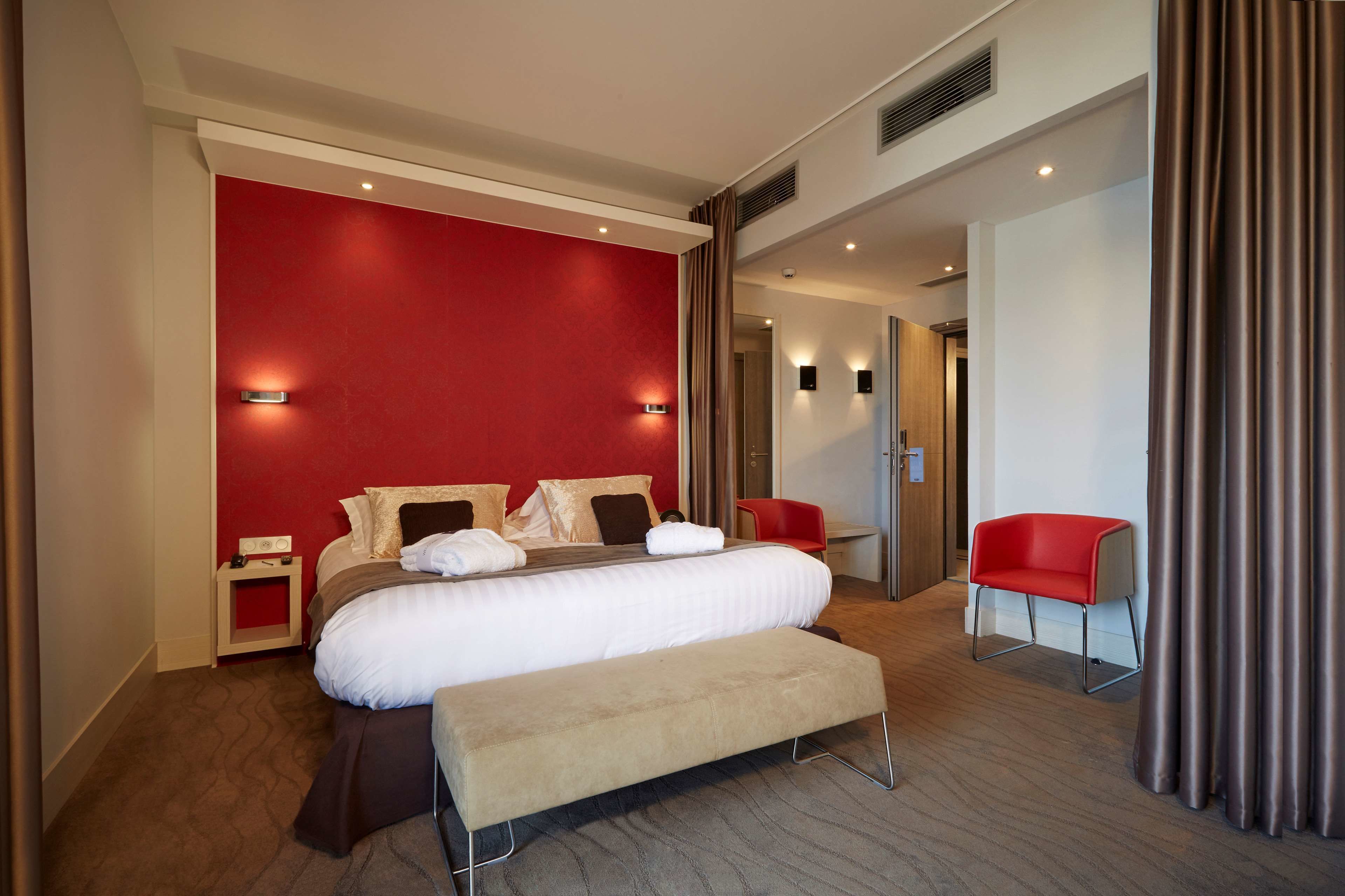 Una habitación de hotel moderna con una cama grande, un banco, una silla roja y una pared decorada en rojo.