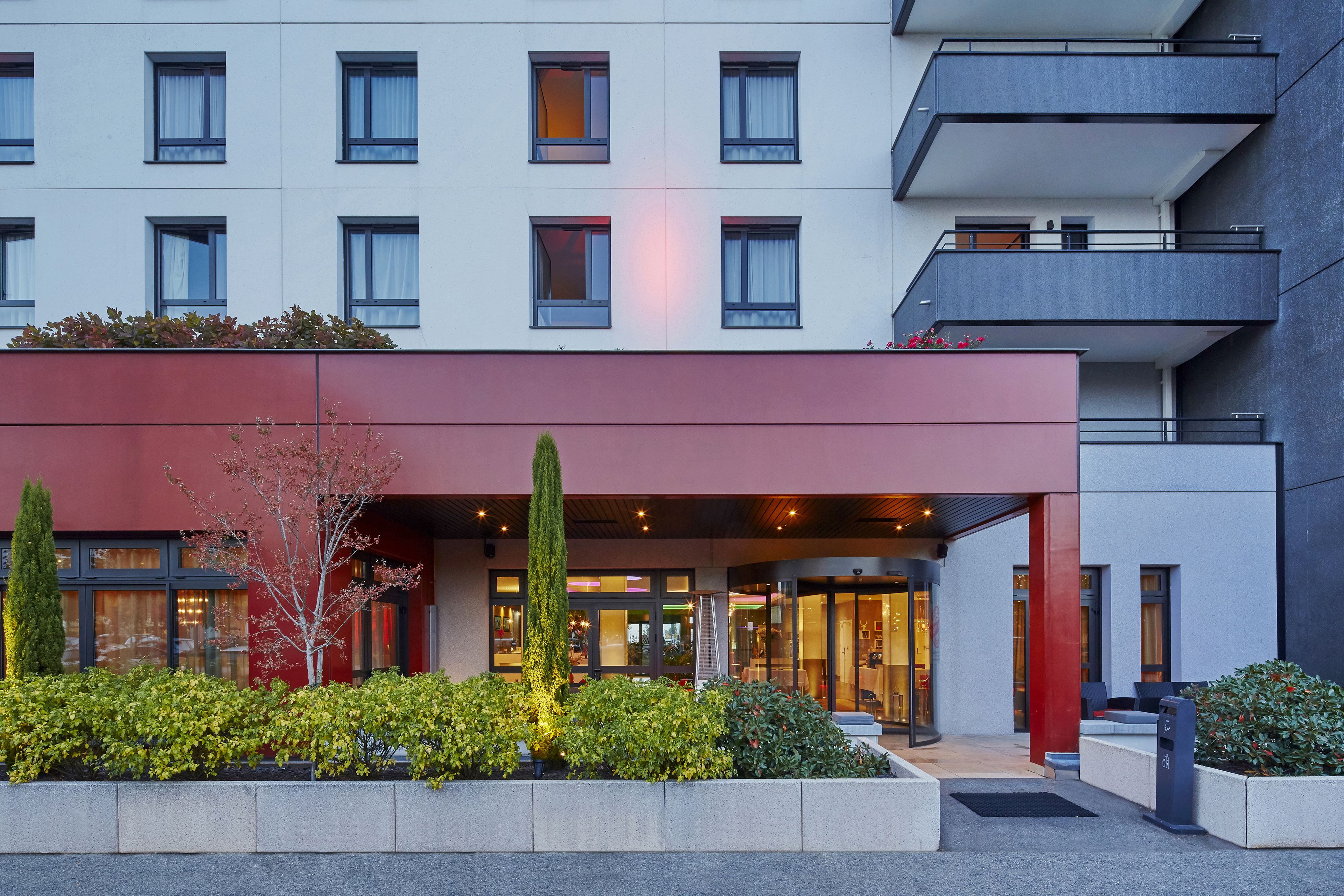 Un hotel moderno con fachada roja, varias ventanas y un jardín bien cuidado.