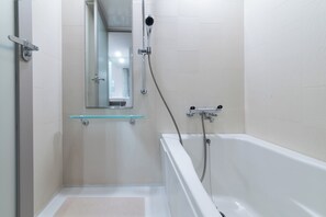 Un baño moderno con repisa de vidrio, ducha con cabezal de ducha manual y bañera.