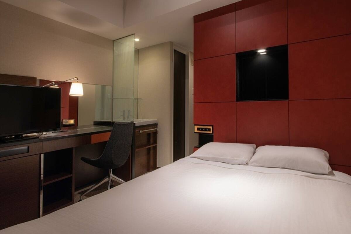 A hotel room with a bed, a desk with a chair, a TV, and a mirror.