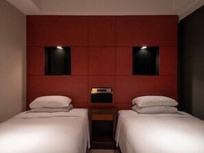 Habitación de hotel con dos camas, una pared de acento roja y una mesita de noche pequeña con lámpara.