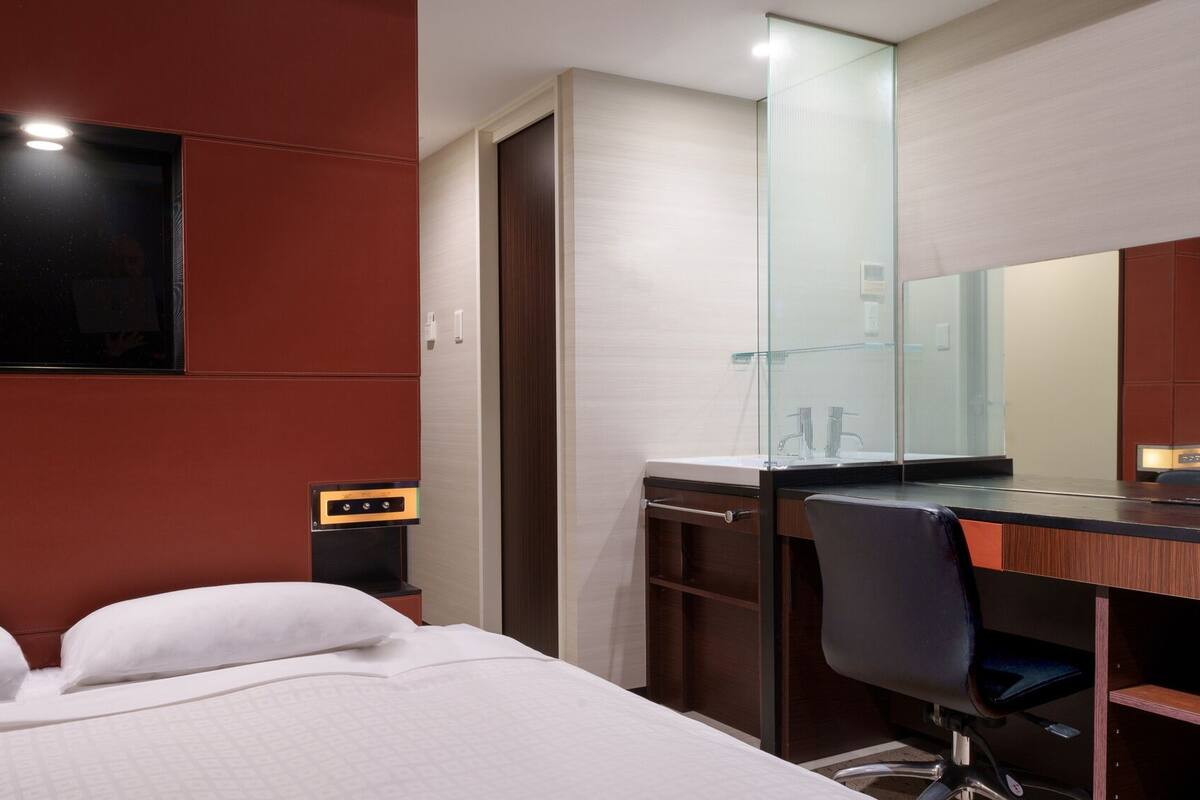 A hotel room with a bed, a desk, a mirror, and a wardrobe.