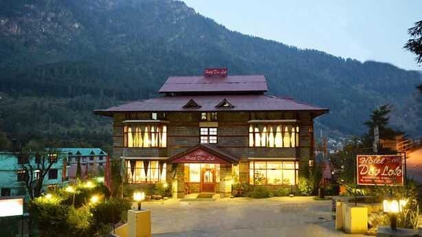 A two-story hotel with a red roof and stone facade, located in a mountainous area. - Hotel Devlok (Manali)