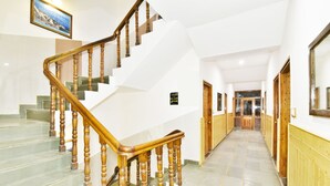 A hotel hallway with a wooden staircase, a framed picture on the wall, and a sign indicating the room number. - Hotel Devlok (Manali)