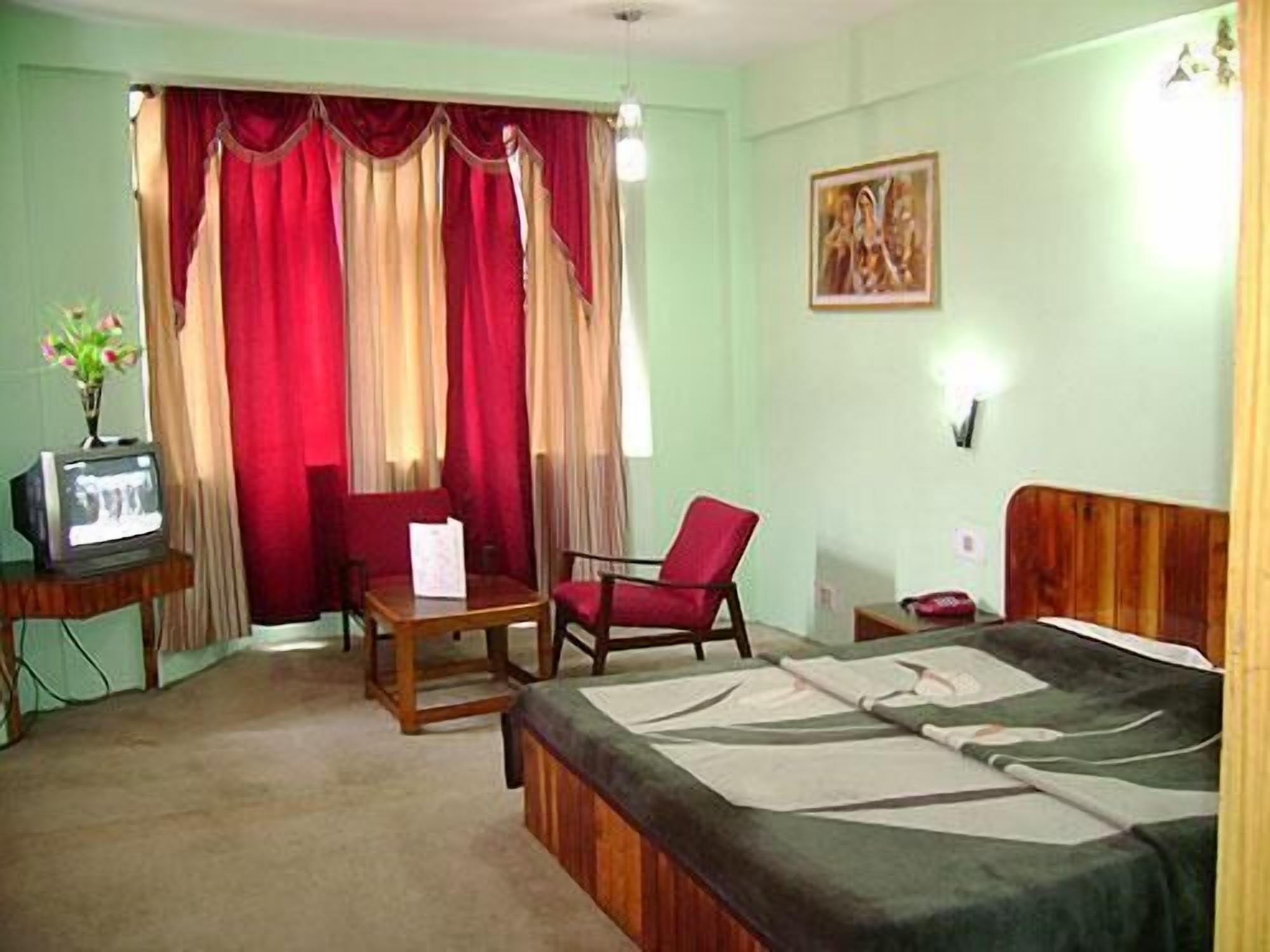Una habitación de hotel con una cama, un escritorio con una silla, un televisor y cortinas.