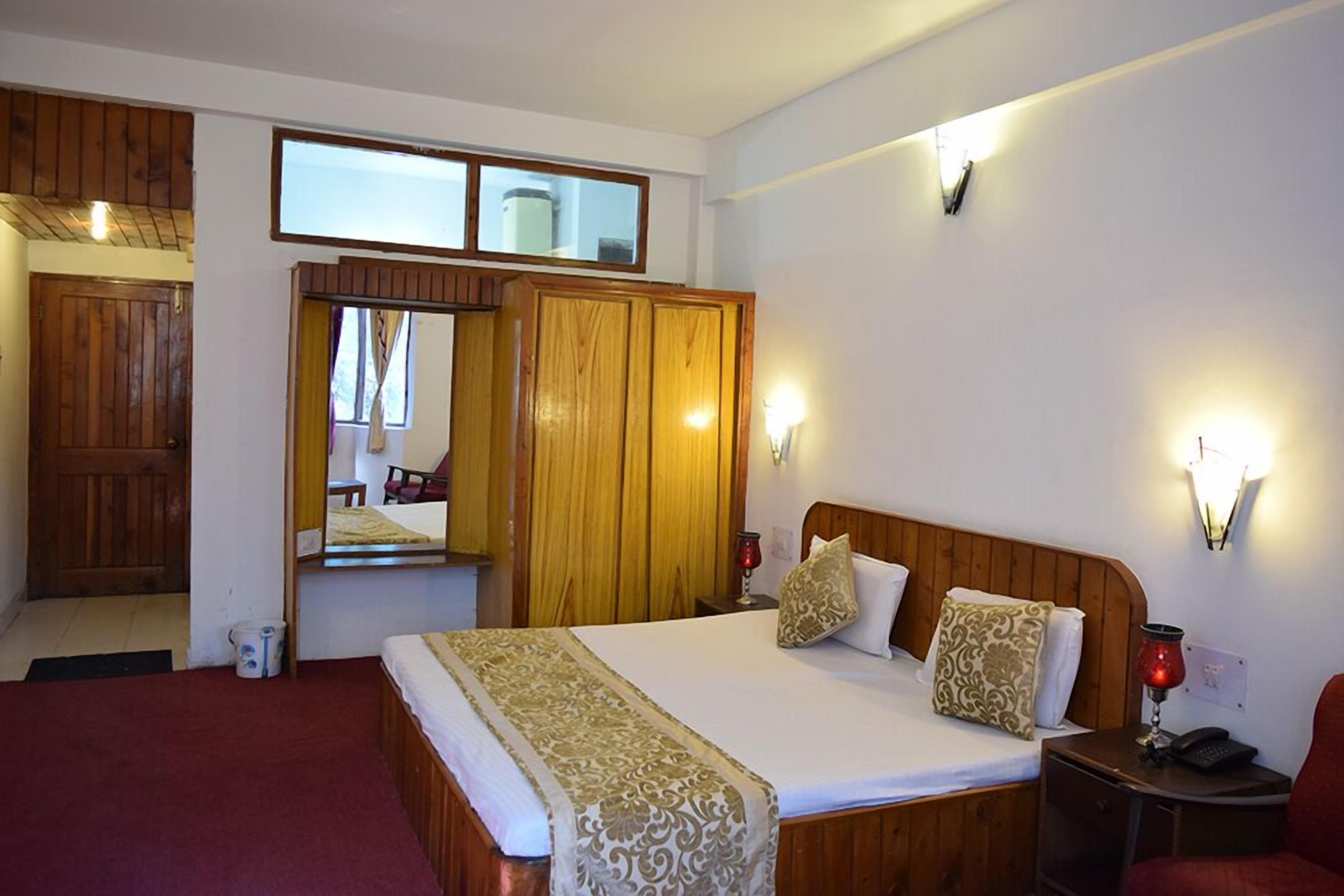A hotel room with a wooden bed, a mirror, a wardrobe, and a small table with a lamp.
