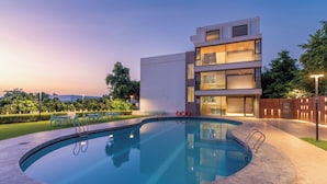 A modern building with a swimming pool, outdoor seating, and a well-lit entrance.