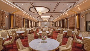 A spacious banquet hall with round tables, plush chairs, and a chandelier.