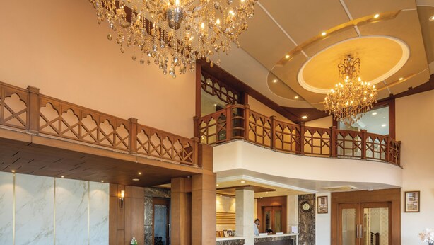 A spacious lobby with a grand chandelier, a reception desk, and a seating area with sofas and armchairs.
