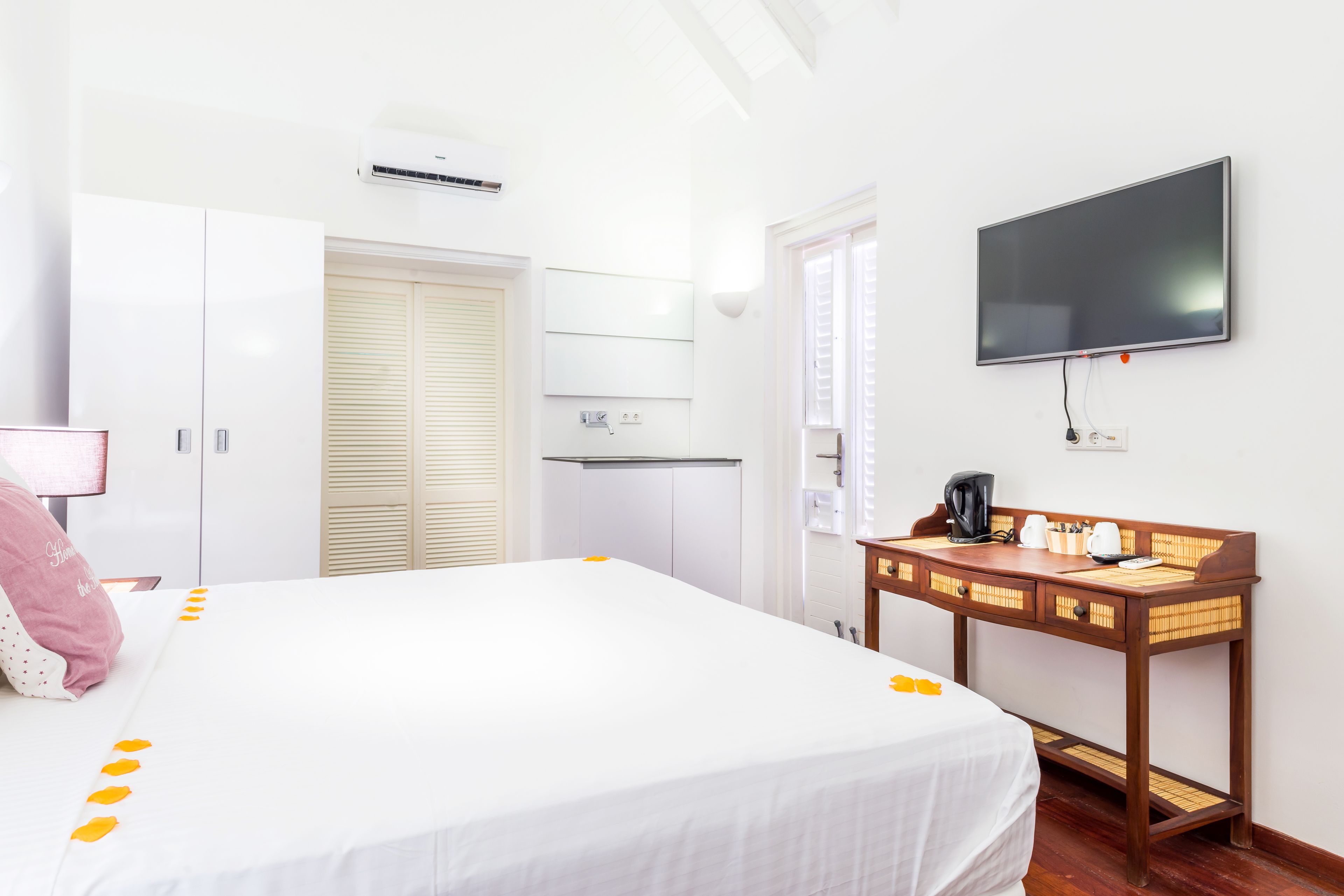 A hotel room with a large bed, a wooden desk with a flat-screen TV, a wardrobe, and a window with blinds.