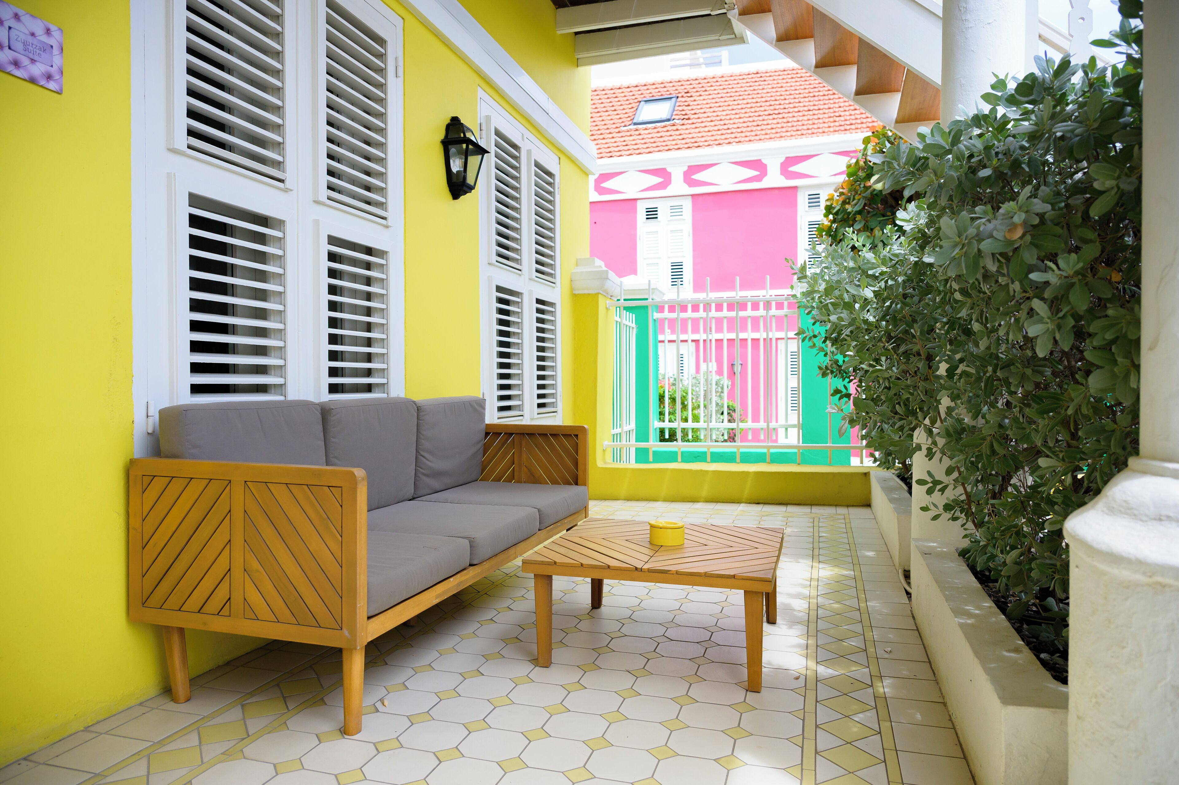 Pared amarilla con contraventanas blancas, un sofá gris y una mesa de madera con una taza amarilla.