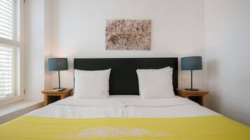 Habitación de hotel con una cama, dos mesitas de noche, un ventanal con persianas y una obra de arte colgada en la pared.