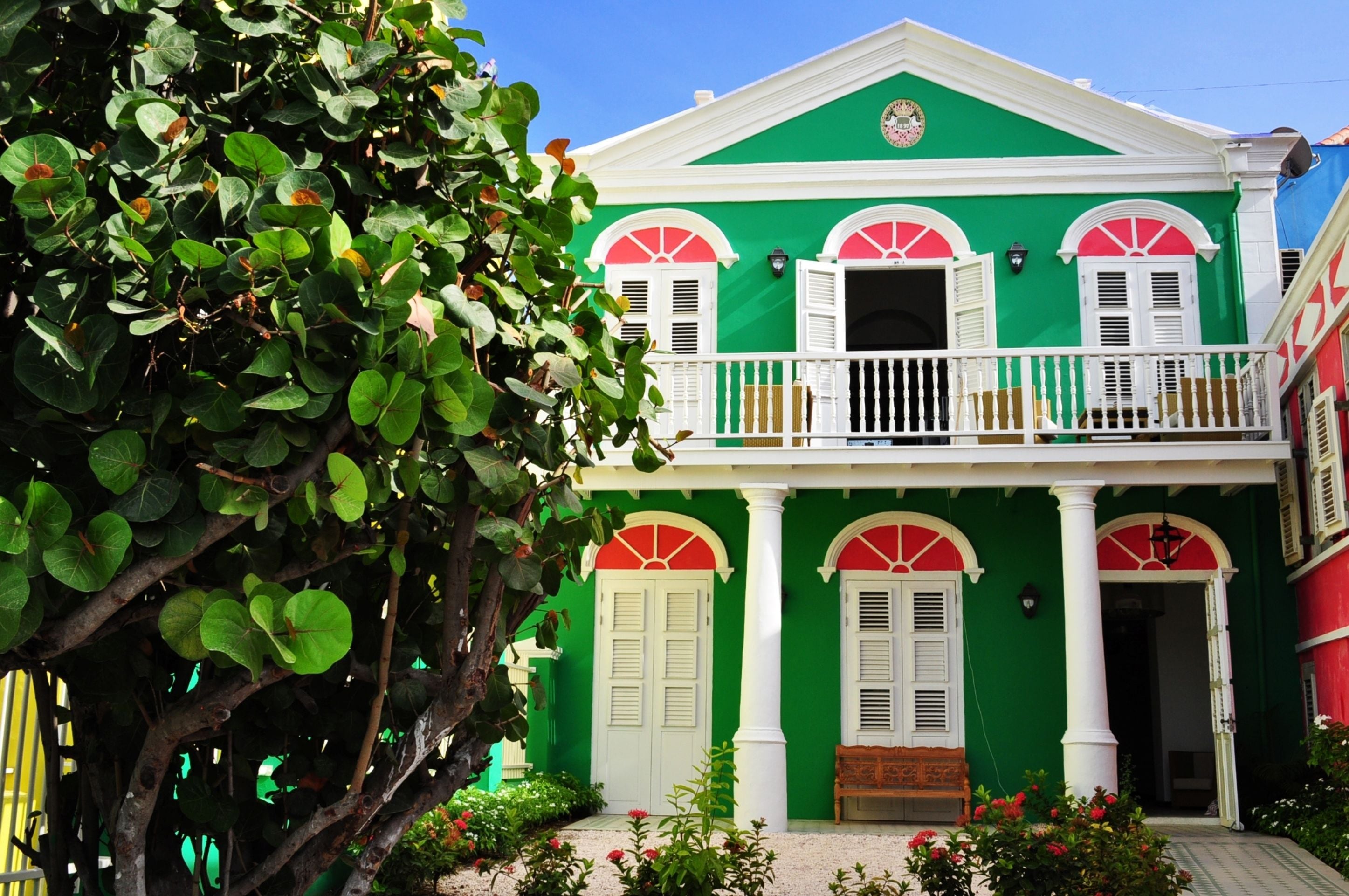 A two-story building with a green facade, white shutters, and a balcony with a wooden railing.