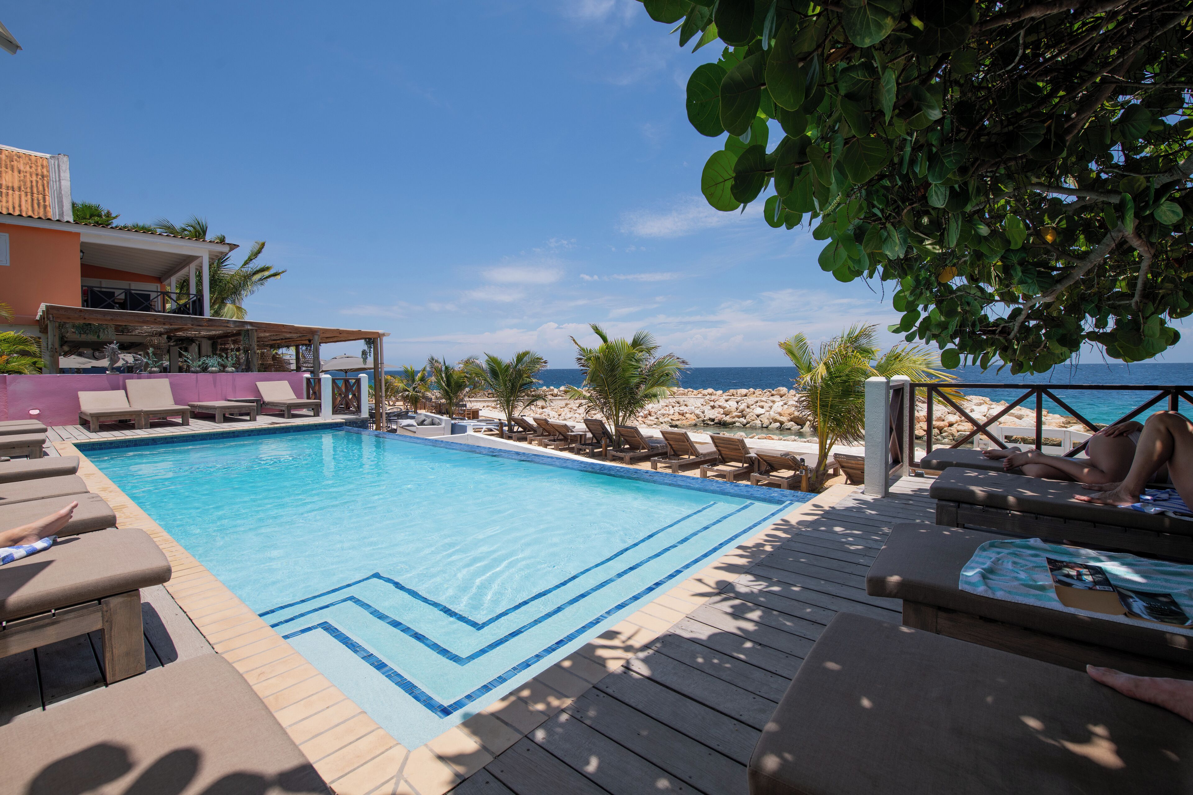 A pool area with lounge chairs and a view of the ocean.