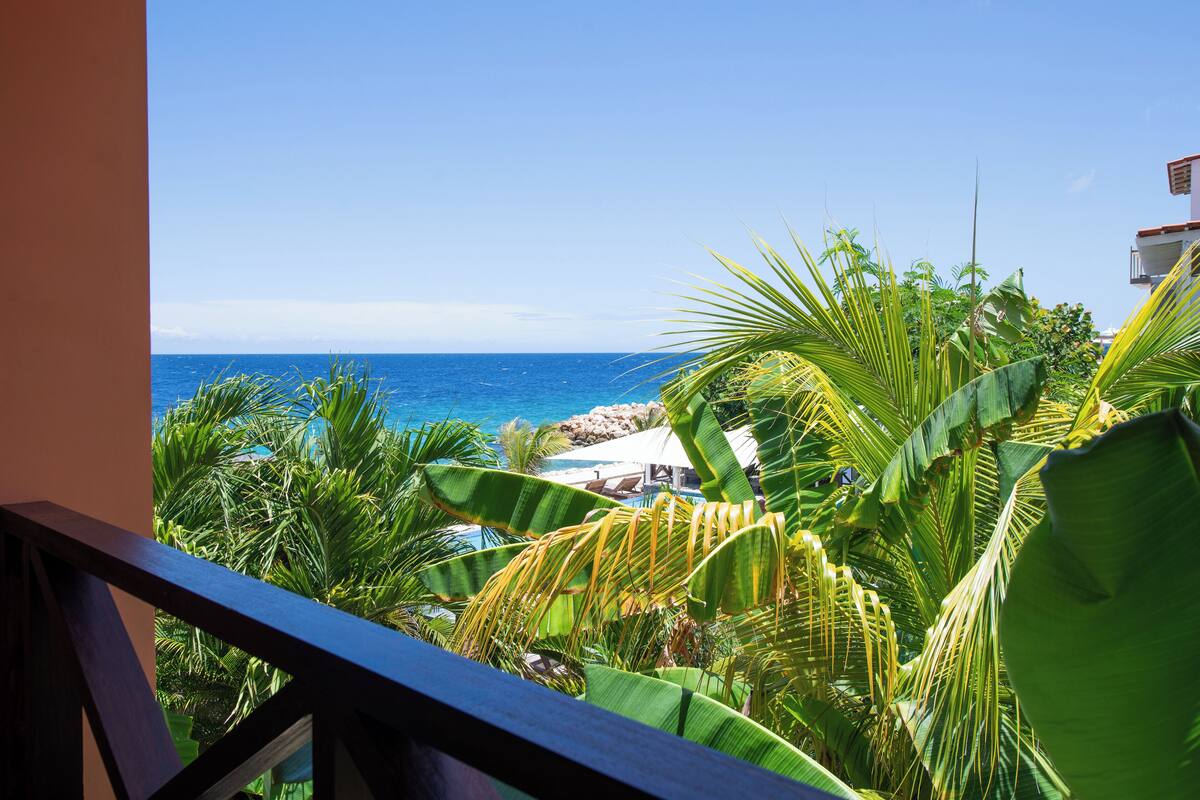A balcony with a view of the ocean and tropical vegetation.