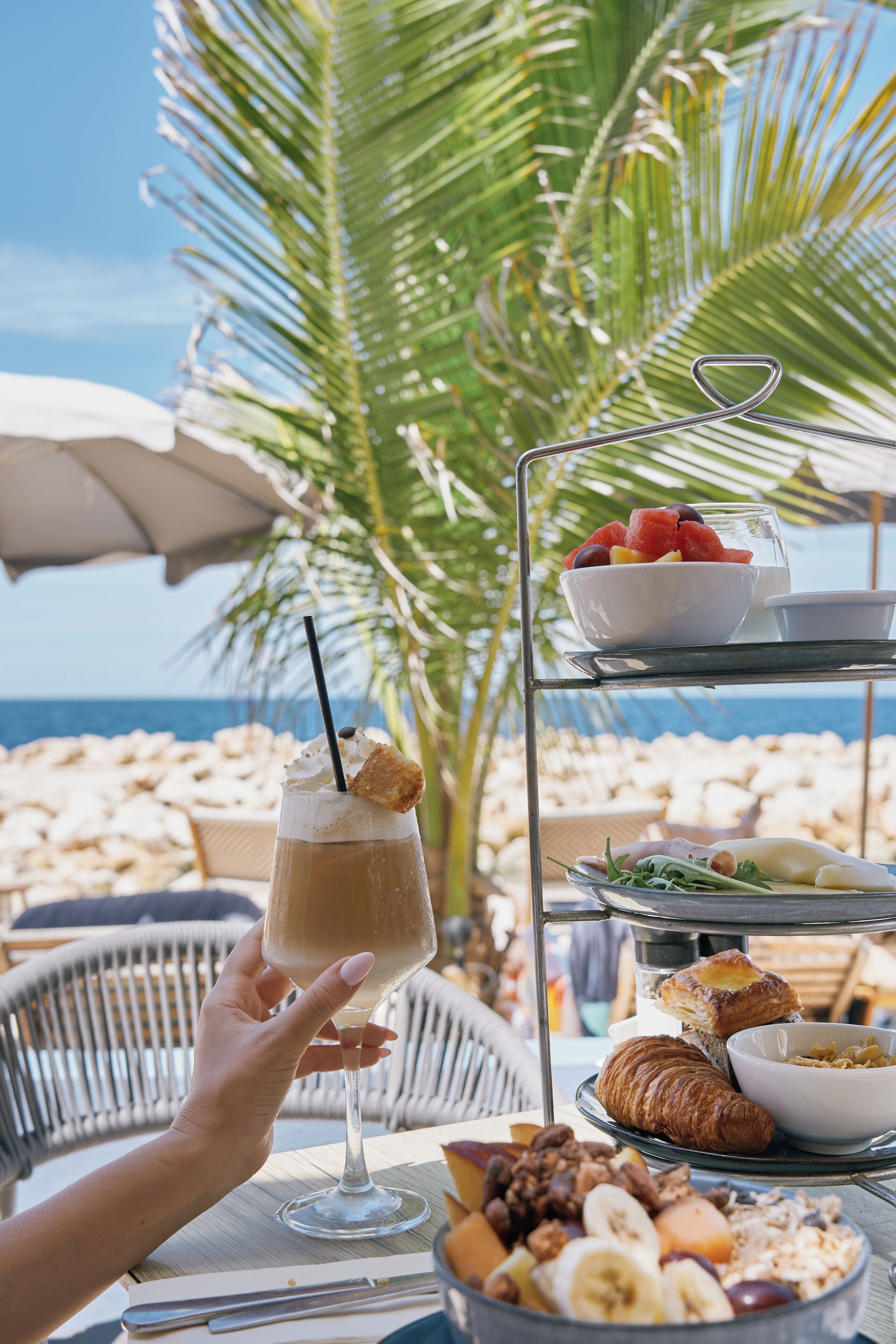 A beachside breakfast setup with a drink, croissants, and fruit.