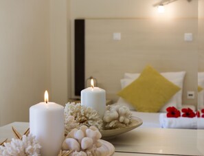 Una habitación con dos velas encendidas, un cuenco de flores decorativas y una cama con un almohadón amarillo.