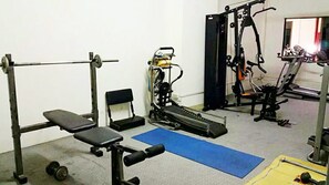 A gym with a bench press, squat rack, and various exercise machines. - Poonchock Mansion (Bangkok)