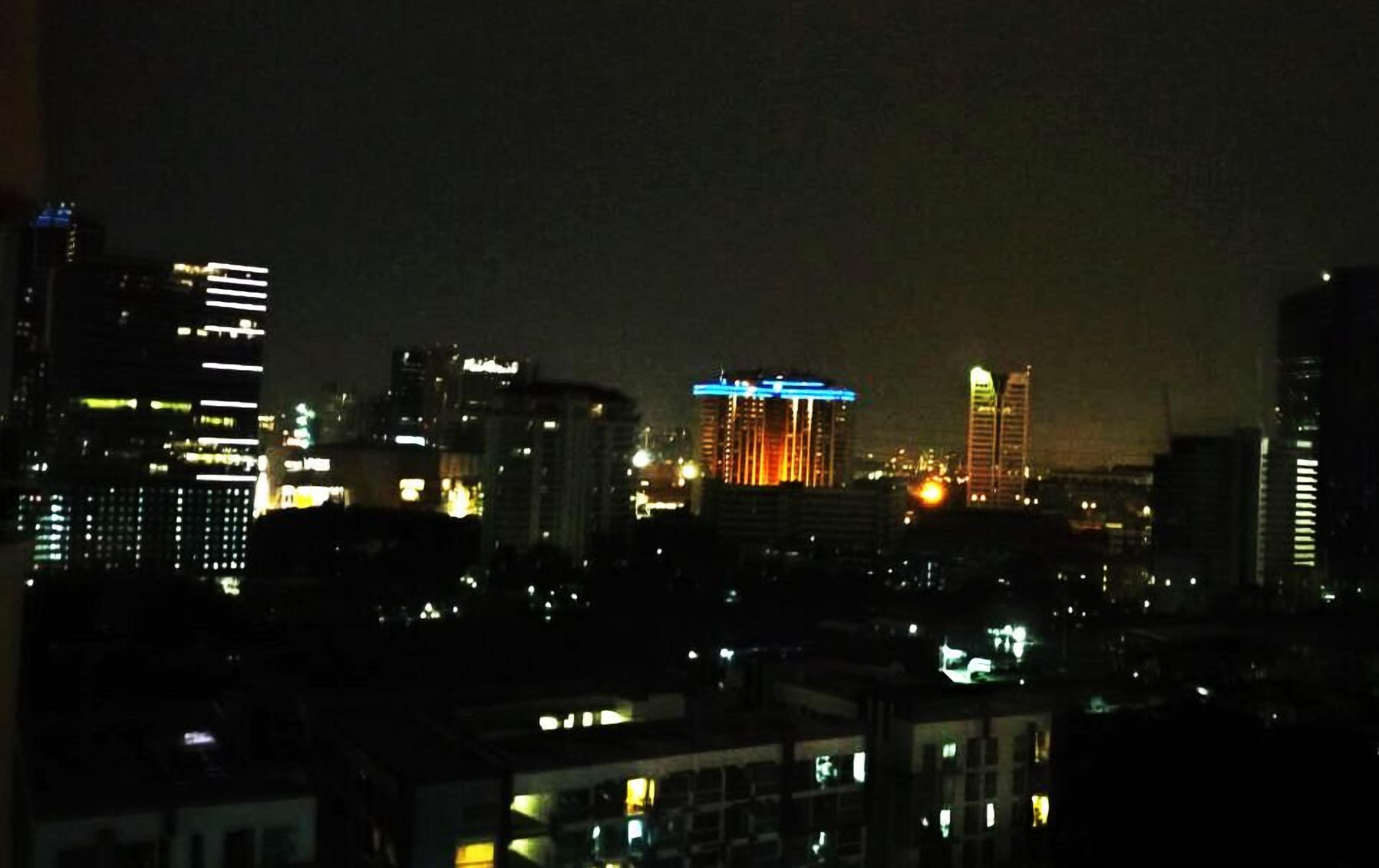 A nighttime cityscape with illuminated buildings, including a prominent hotel with a lit blue sign.