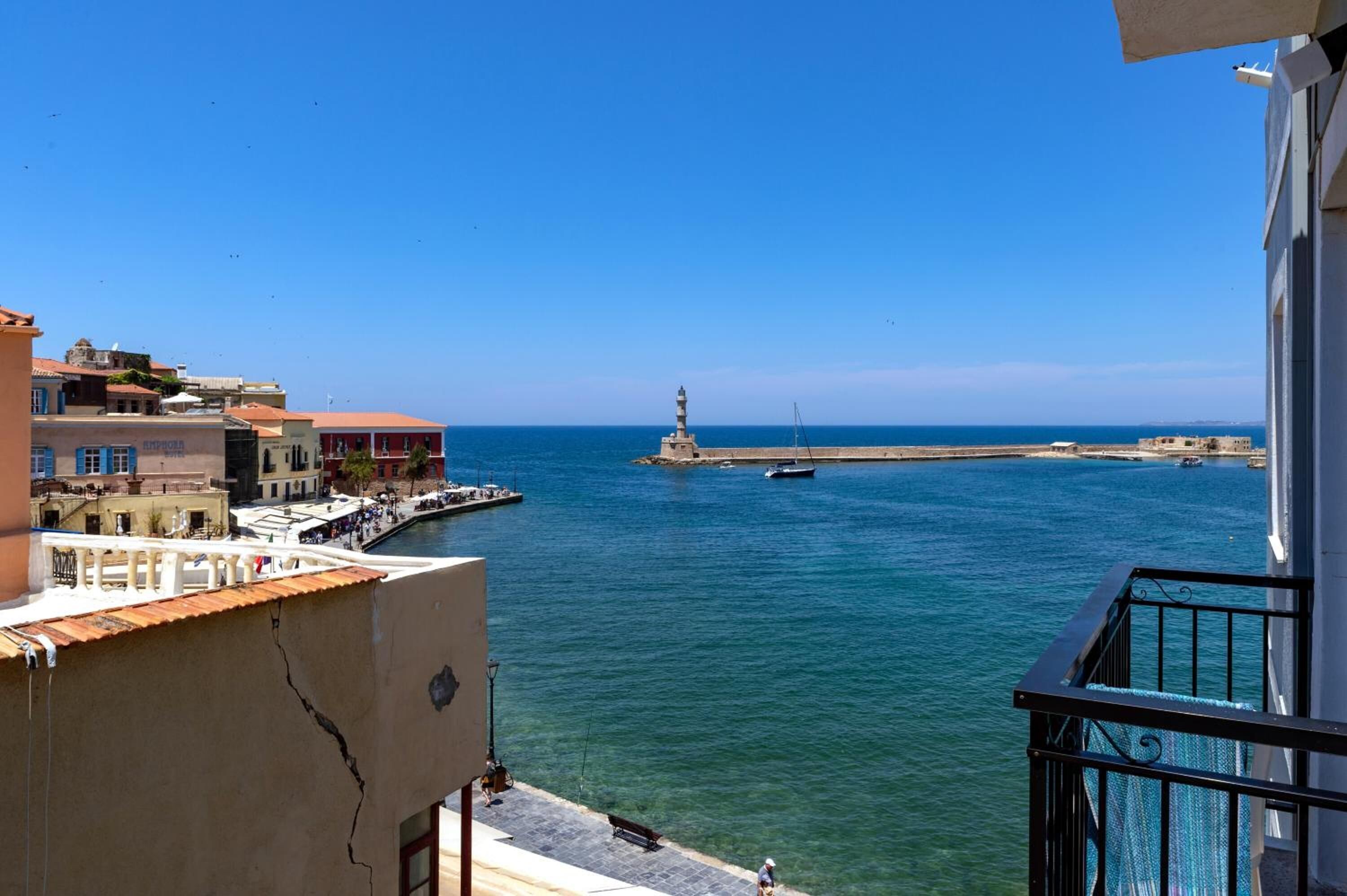 A coastal view from a balcony overlooking a marina with boats, a lighthouse, and buildings along the shore.