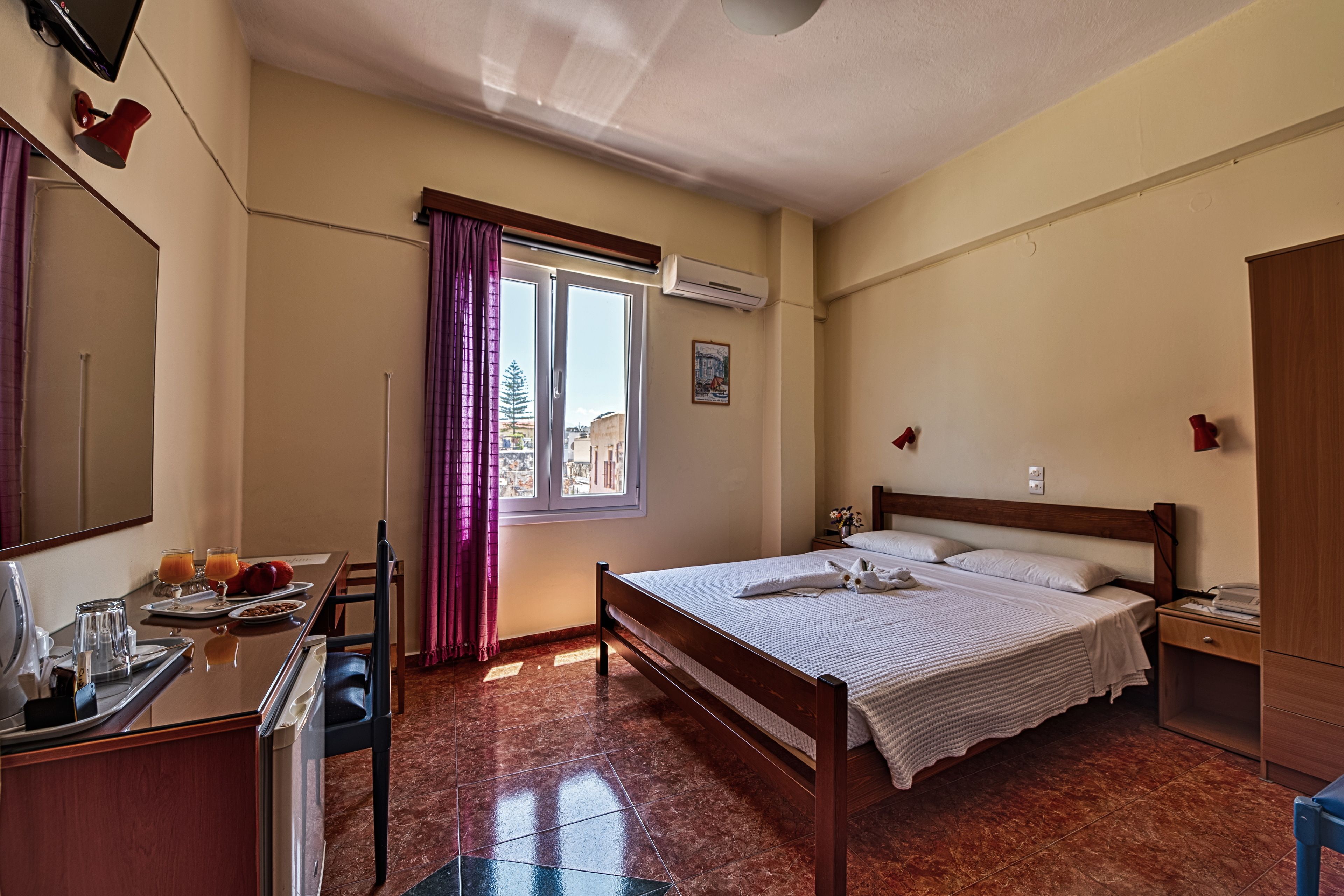 Une chambre d’hôtel avec un lit, une table de chevet, un bureau et une fenêtre avec des rideaux.