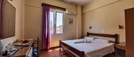 A hotel room with a bed, bedside table, desk, and a window with curtains.