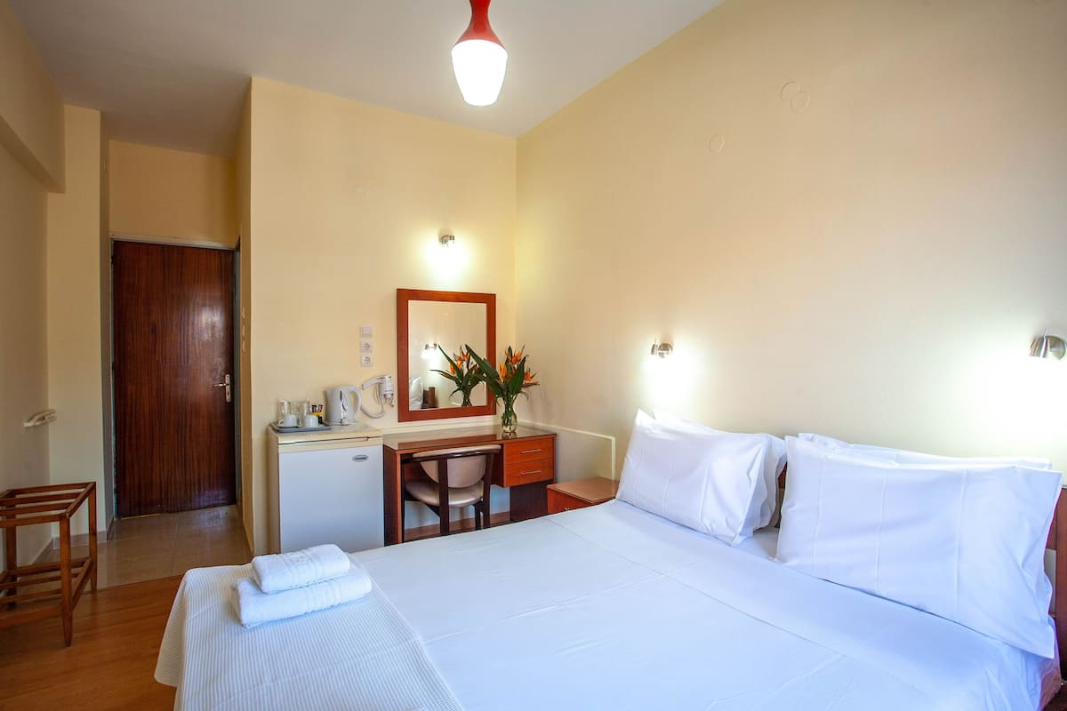 A hotel room with a bed, a desk, a chair, a mirror, and a small cabinet.