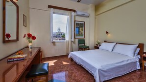 Habitación de hotel con cama, escritorio con silla, ventana con vistas y un cuadro en la pared.