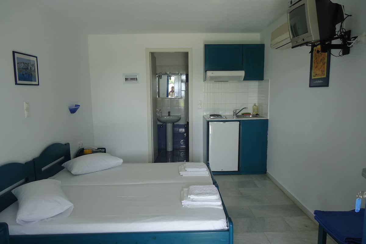Une chambre avec un lit, une petite kitchenette et une salle de bain visible à travers une porte ouverte.