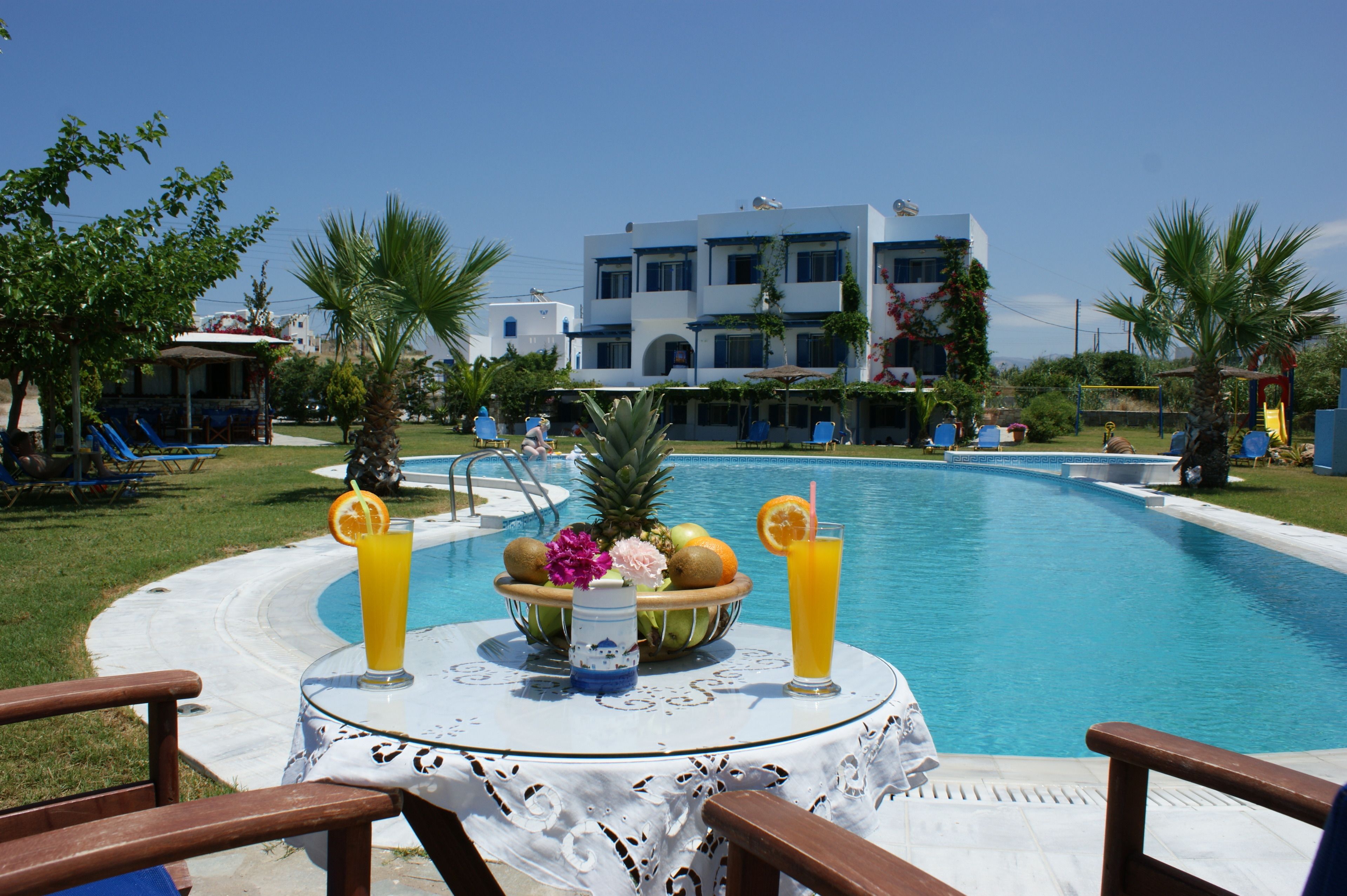 A poolside table with fruit and drinks, surrounded by lounge chairs and a pool.