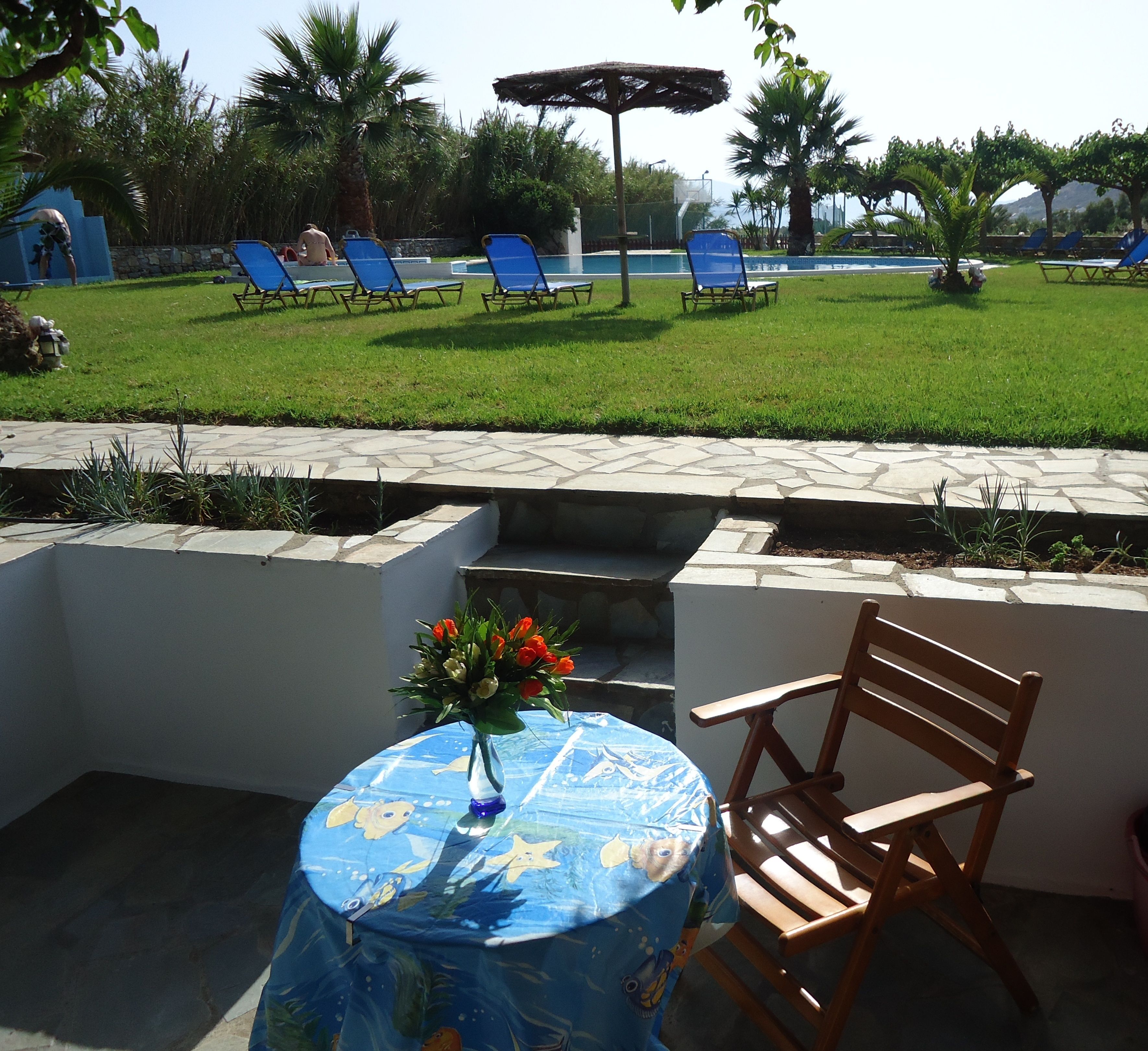 An outdoor patio with a round table, a wooden chair, and a flower vase.