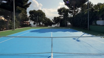 Una cancha de tenis al aire libre con una red en el centro, rodeada de árboles y una valla.