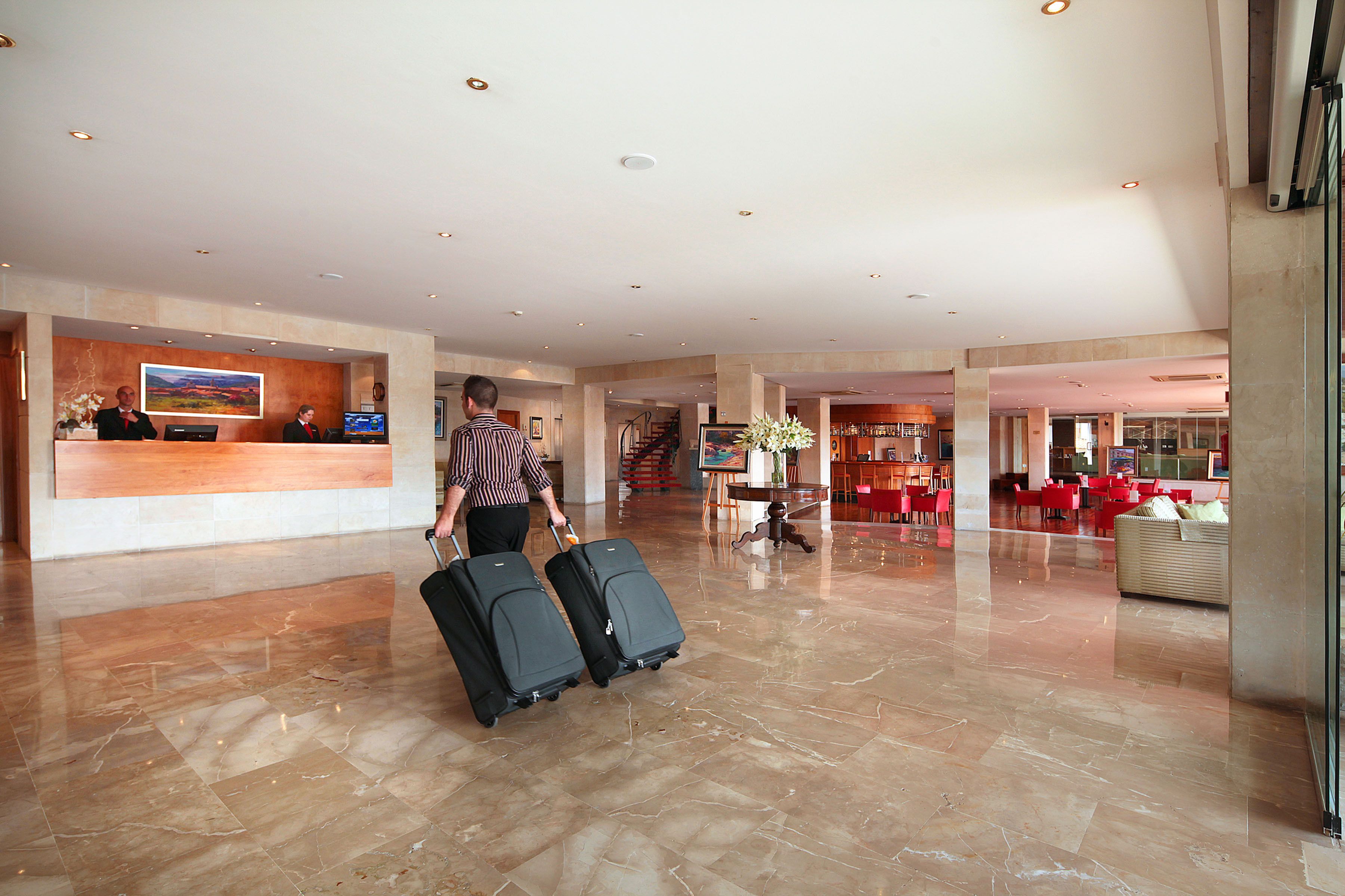 A spacious lobby with a reception desk, a staircase, and a seating area with red chairs.