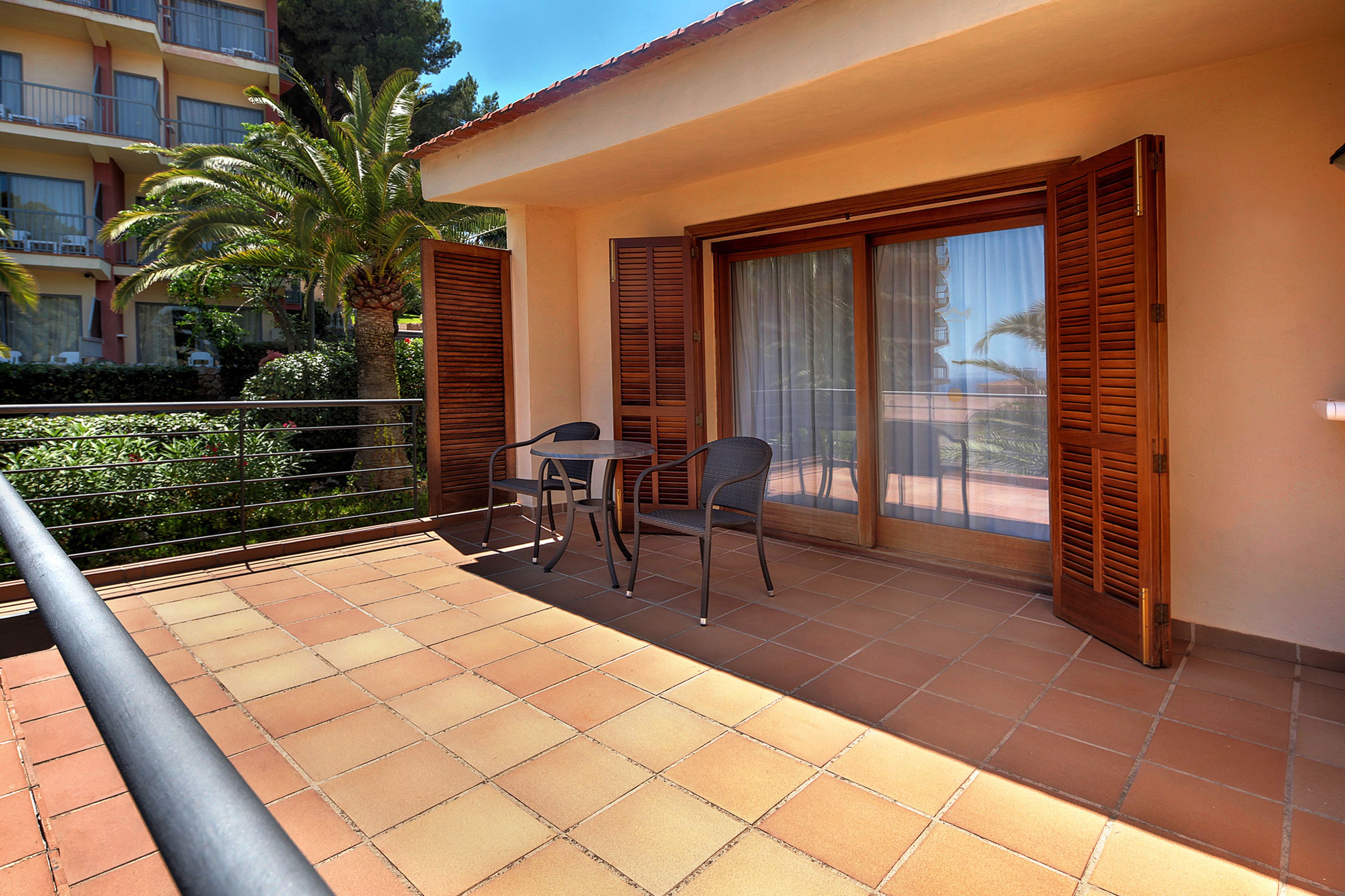 A balcony with a table and chairs, a palm tree, and a view of a building with balconies.