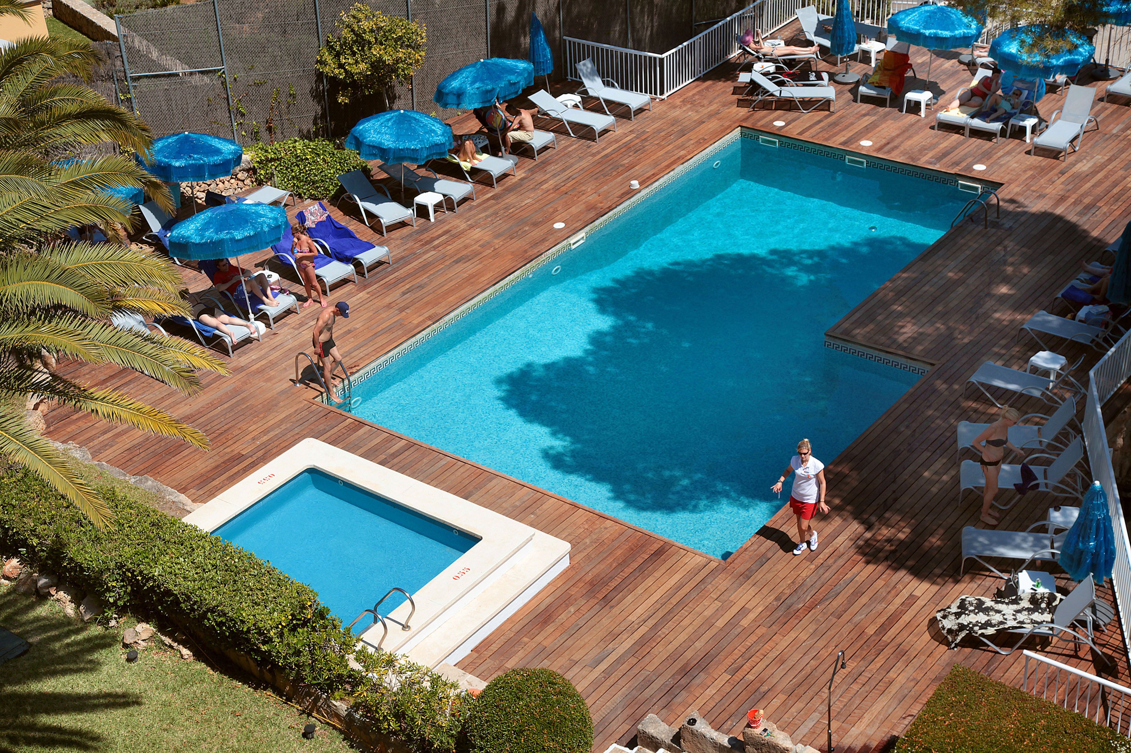 Piscina rectangular con muelle de madera, rodeada de sillas de descanso y sombrillas azules.