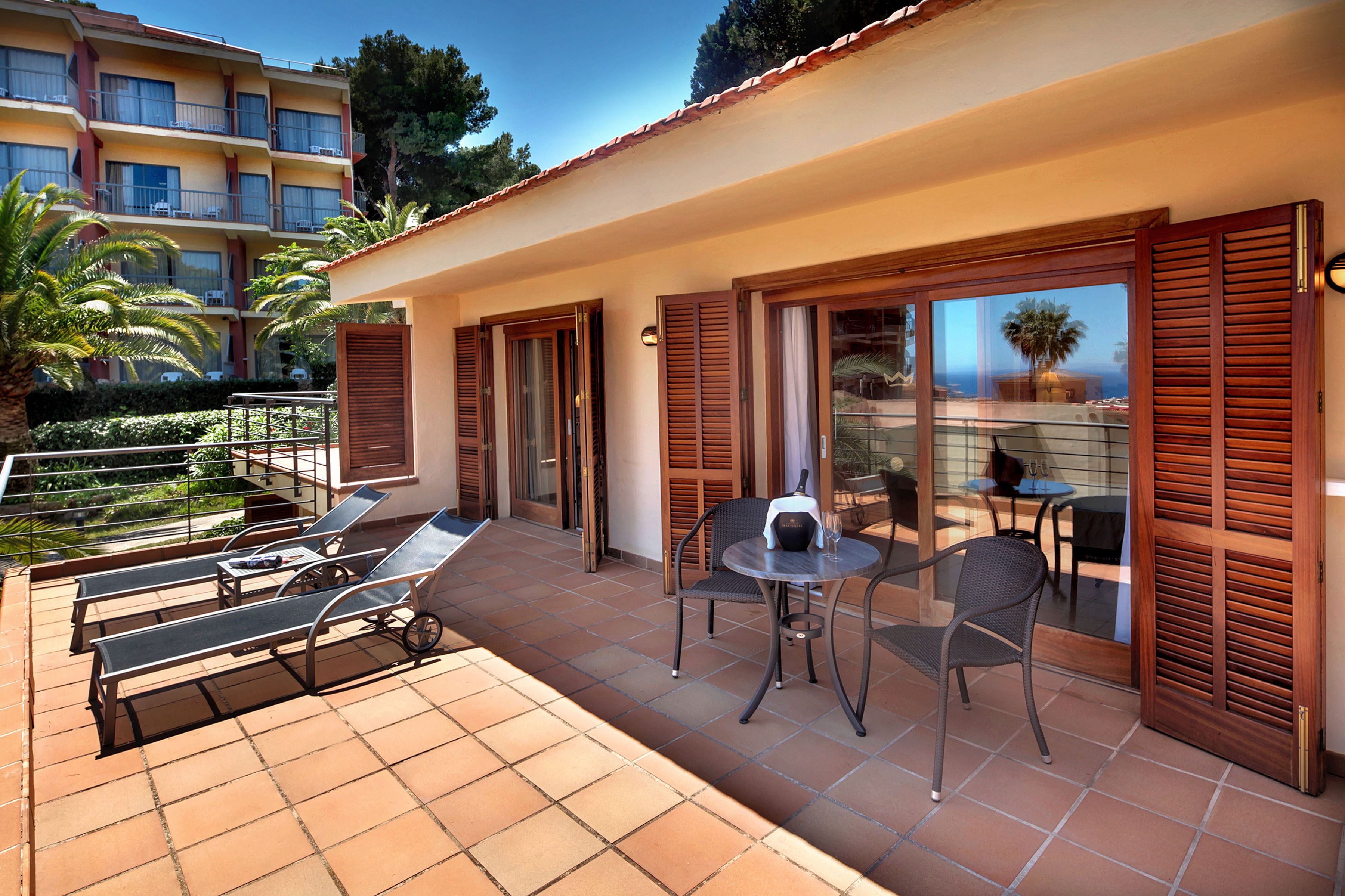 Un balcón de hotel con sillones de sol, una mesa con sillas y vistas al mar.
