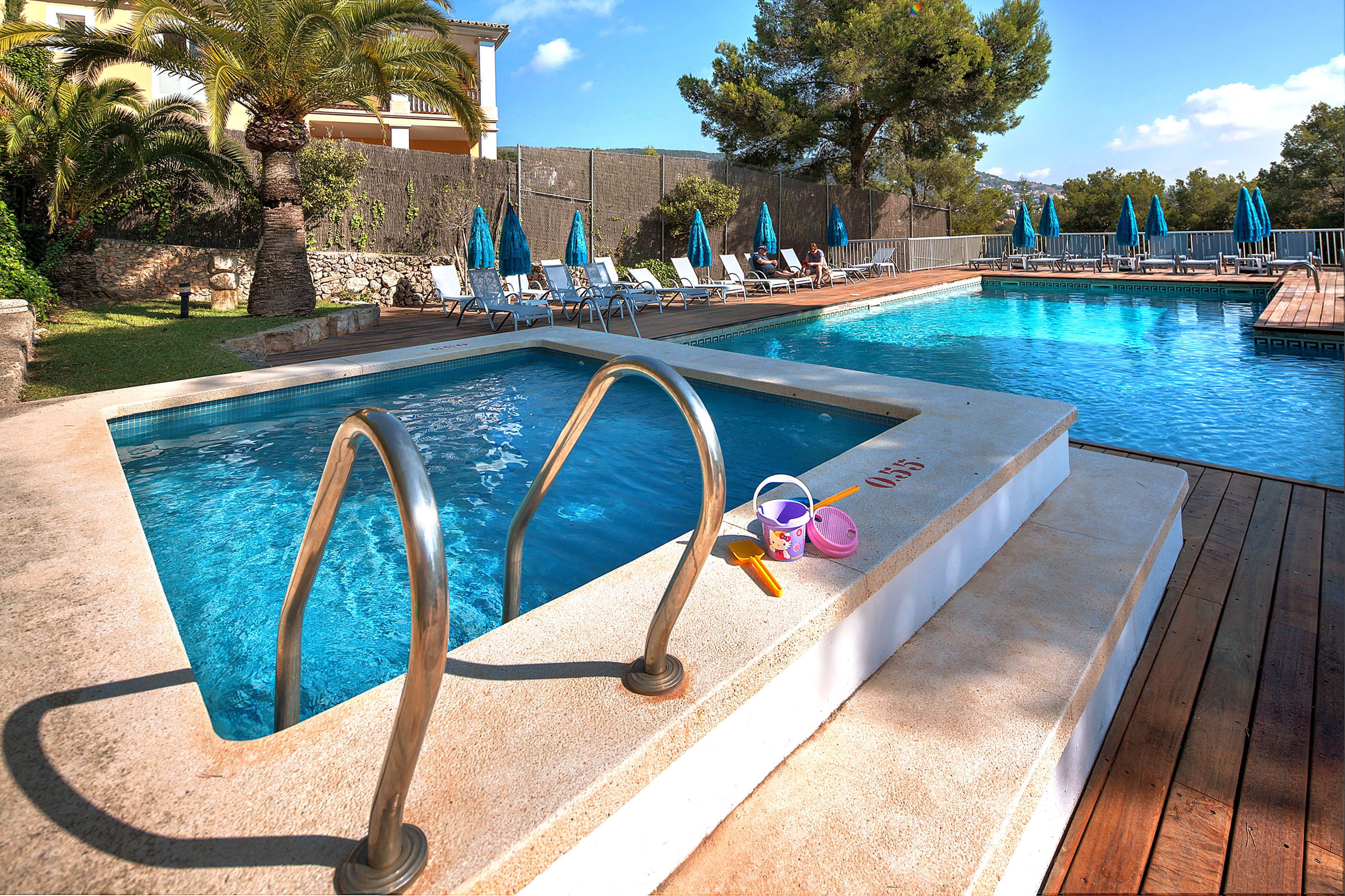 A swimming pool with lounge chairs and umbrellas, surrounded by a wooden deck and greenery.