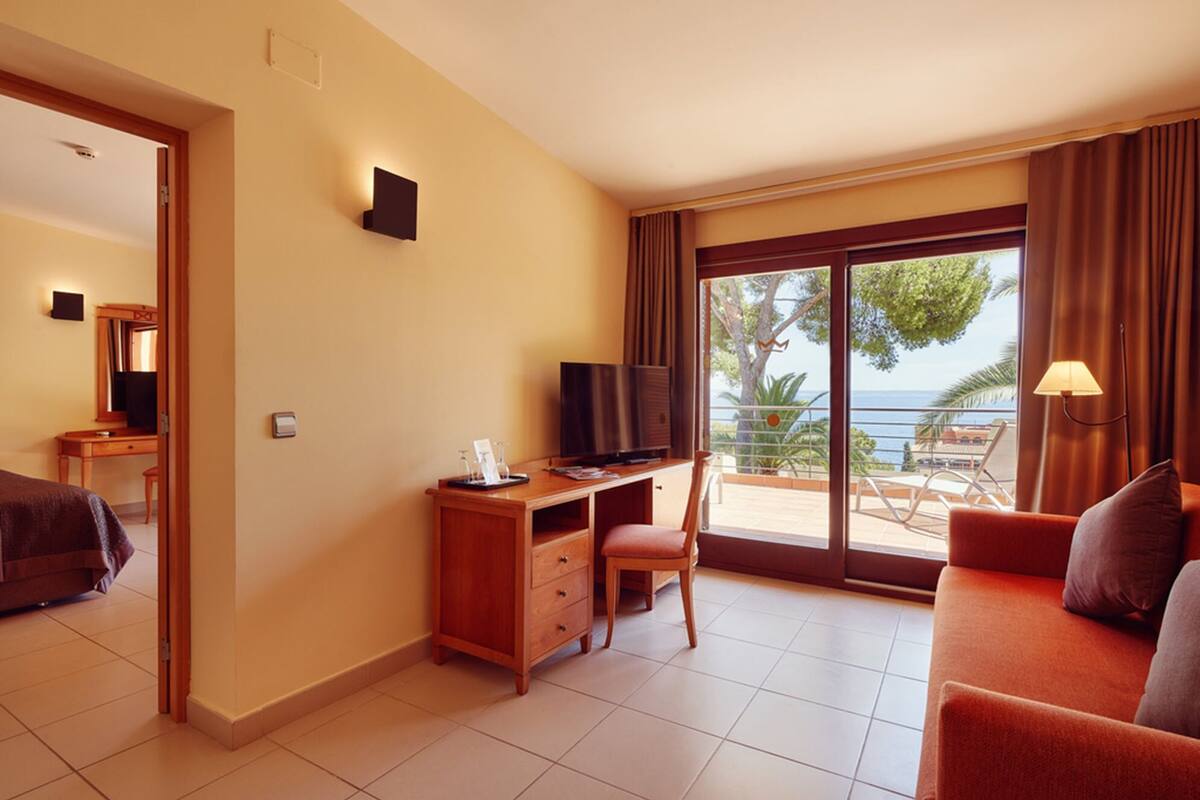 A hotel room with a desk, chair, television, and a sofa.