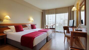 Habitación de hotel con cama doble, escritorio, silla, televisión y ventana con cortinas.