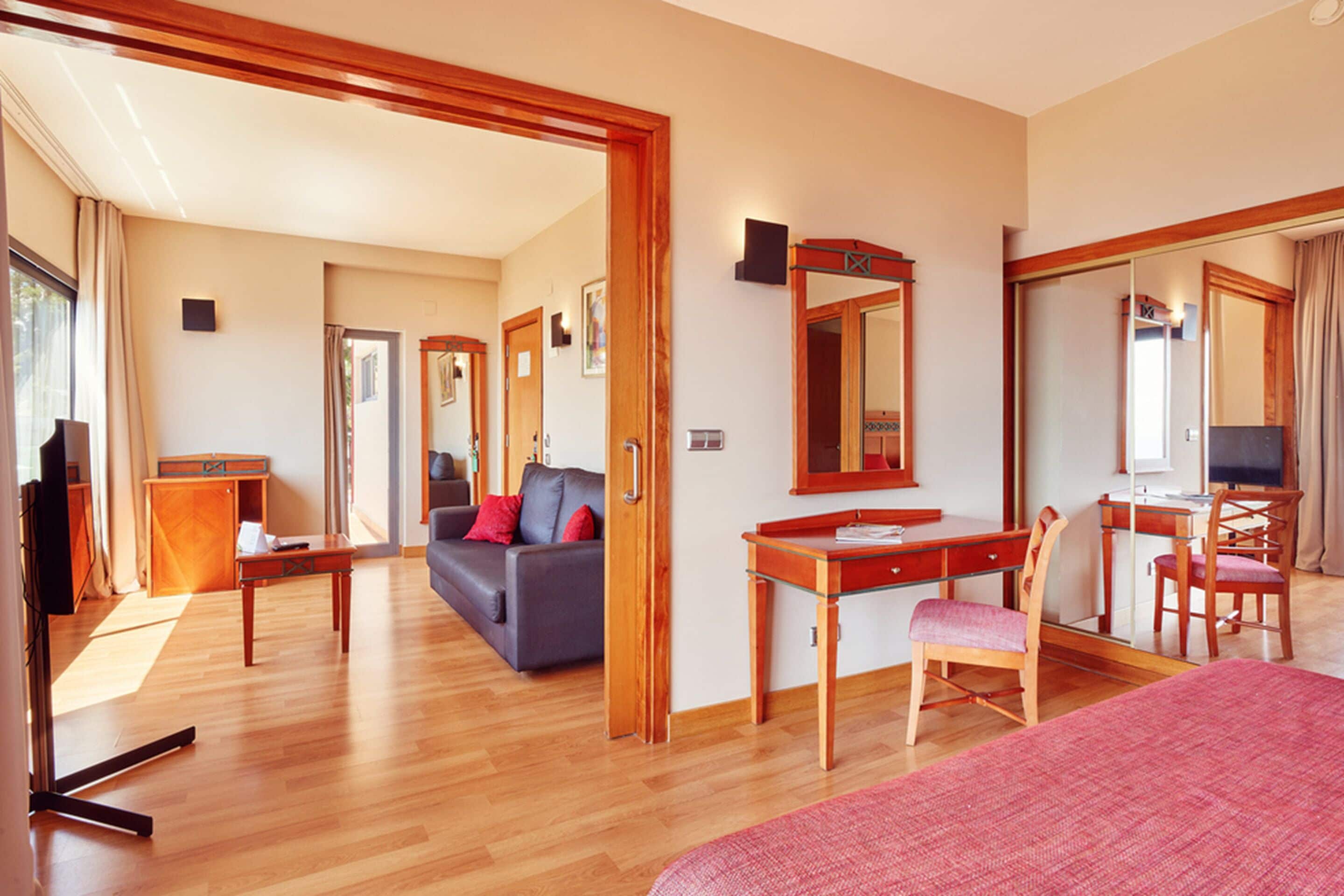 Ein Hotelzimmer mit Holzboden, einem Bett, einem Schreibtisch mit Stuhl, einer Couch und einem Spiegel.