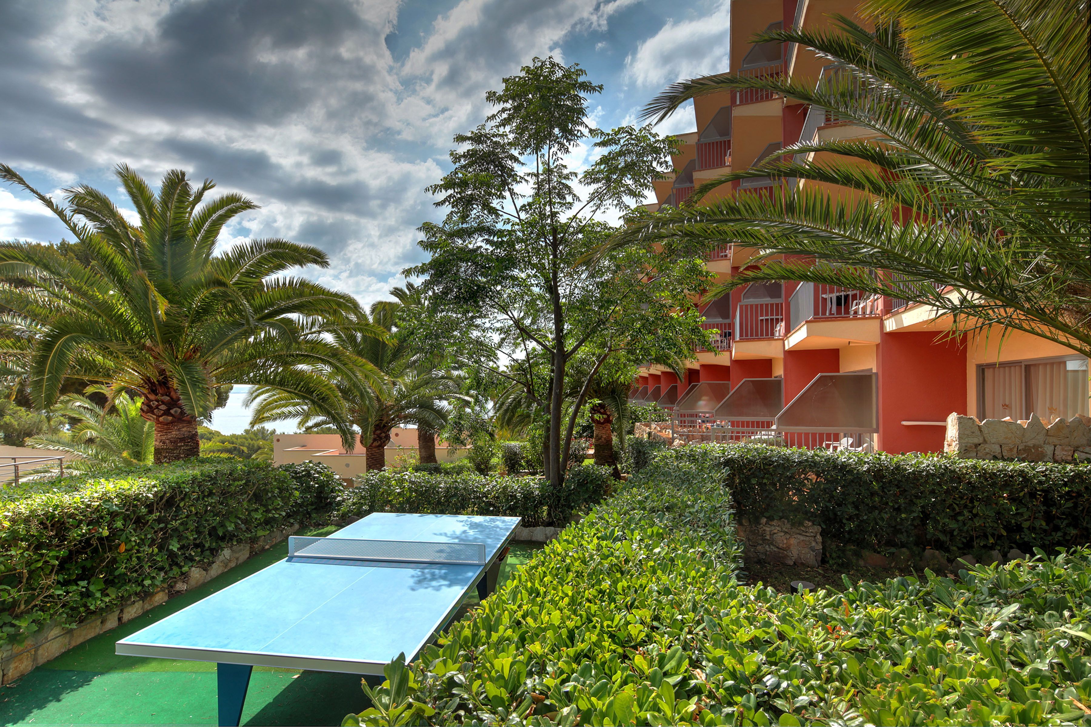 A courtyard with a ping pong table, palm trees, and a building with balconies.