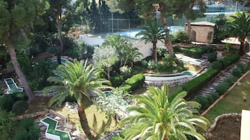 Un jardín exuberante con palmeras, una piscina y una cancha de tenis.