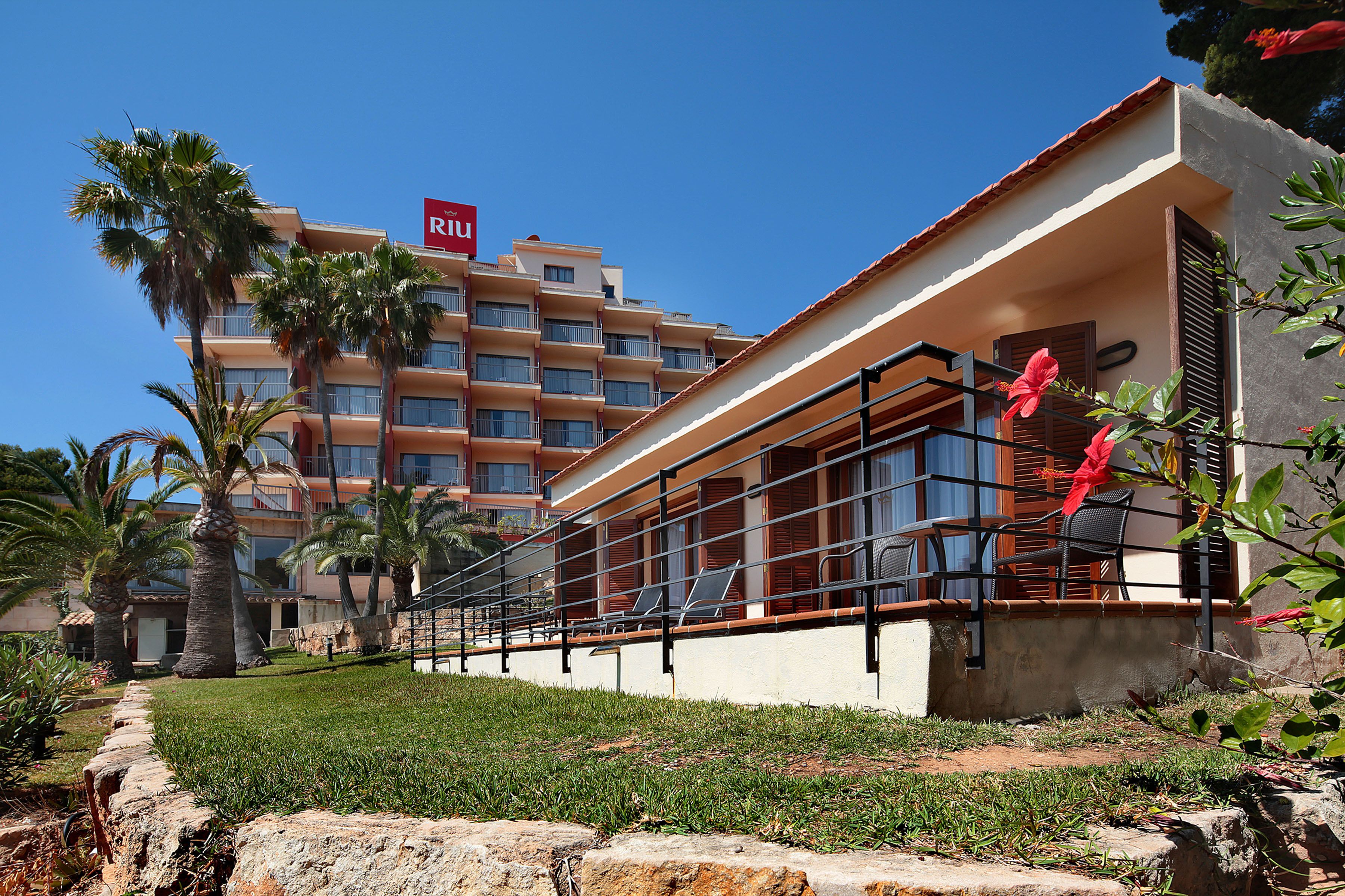 A hotel with a red sign, palm trees, and a balcony with red flowers.